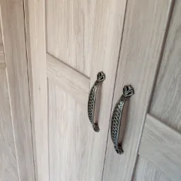 Jasne, drewniane drzwi szafy z ozdobnymi, metalowymi uchwytami w stylu vintage, sfotografowane z bliska pod kątem.