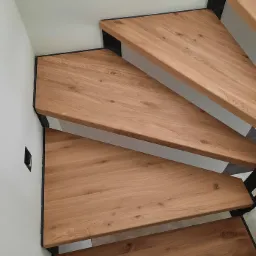 Spiralne, dębowe stopnie z czarną metalową konstrukcją, widok z góry, minimalistyczny design.