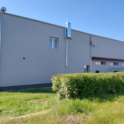 Eryk Konarski - Szary budynek z blachy trapezowej z systemem wentylacyjnym na elewacji, widok z poziomu trawnika. Na rusztowaniu stoi osoba.