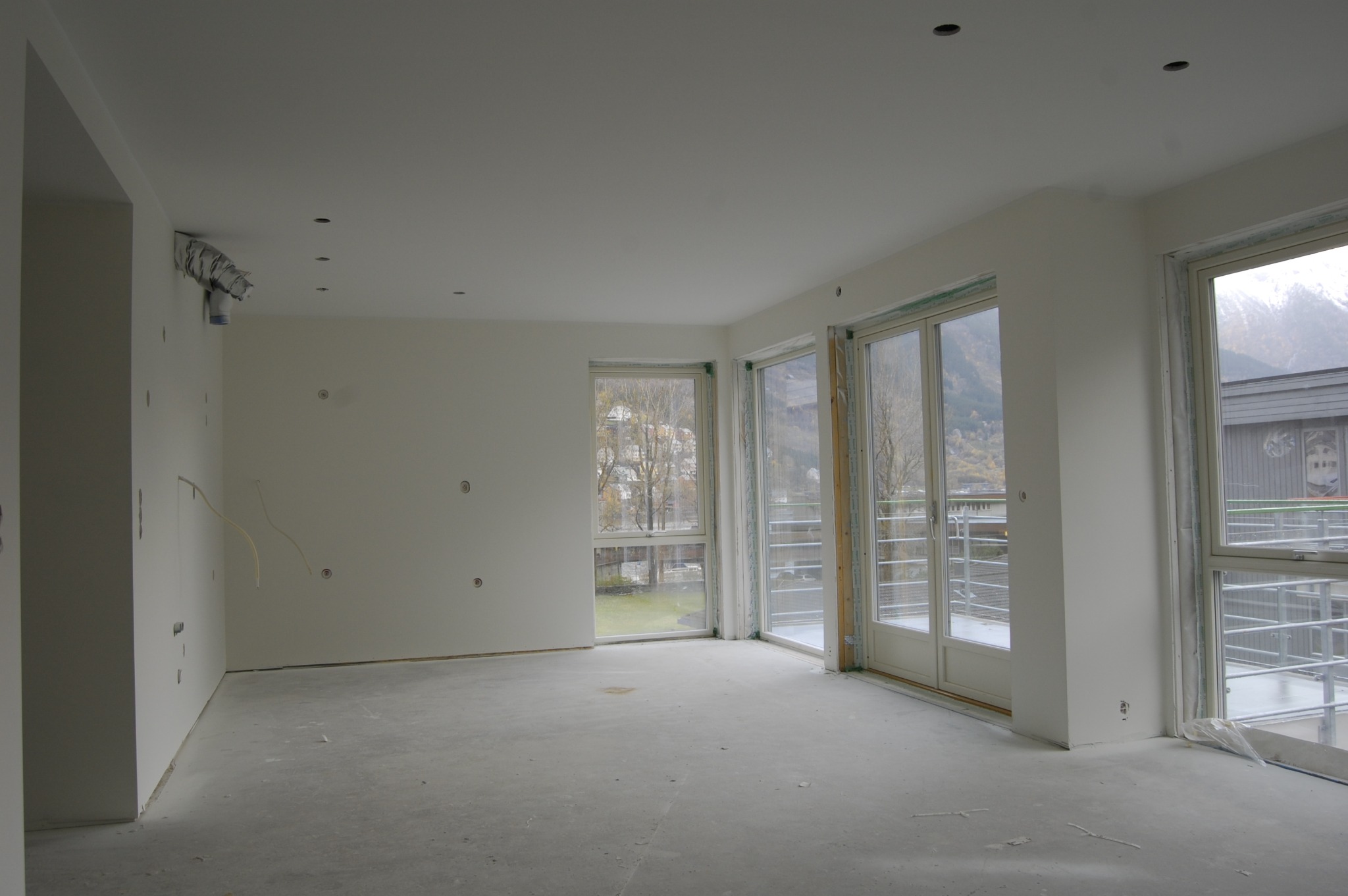 Wnętrze w stanie deweloperskim w Legnicy, ściany przygotowane do malowania z widocznymi punktami elektrycznymi, surowa podłoga, duże okna z widokiem na góry.