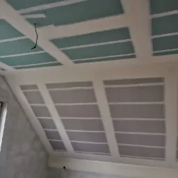 Skośny sufit na poddaszu z zamontowanymi płytami gipsowo-kartonowymi, widoczne łączenia płyt zabezpieczone taśmą, wystający kabel oświetleniowy.