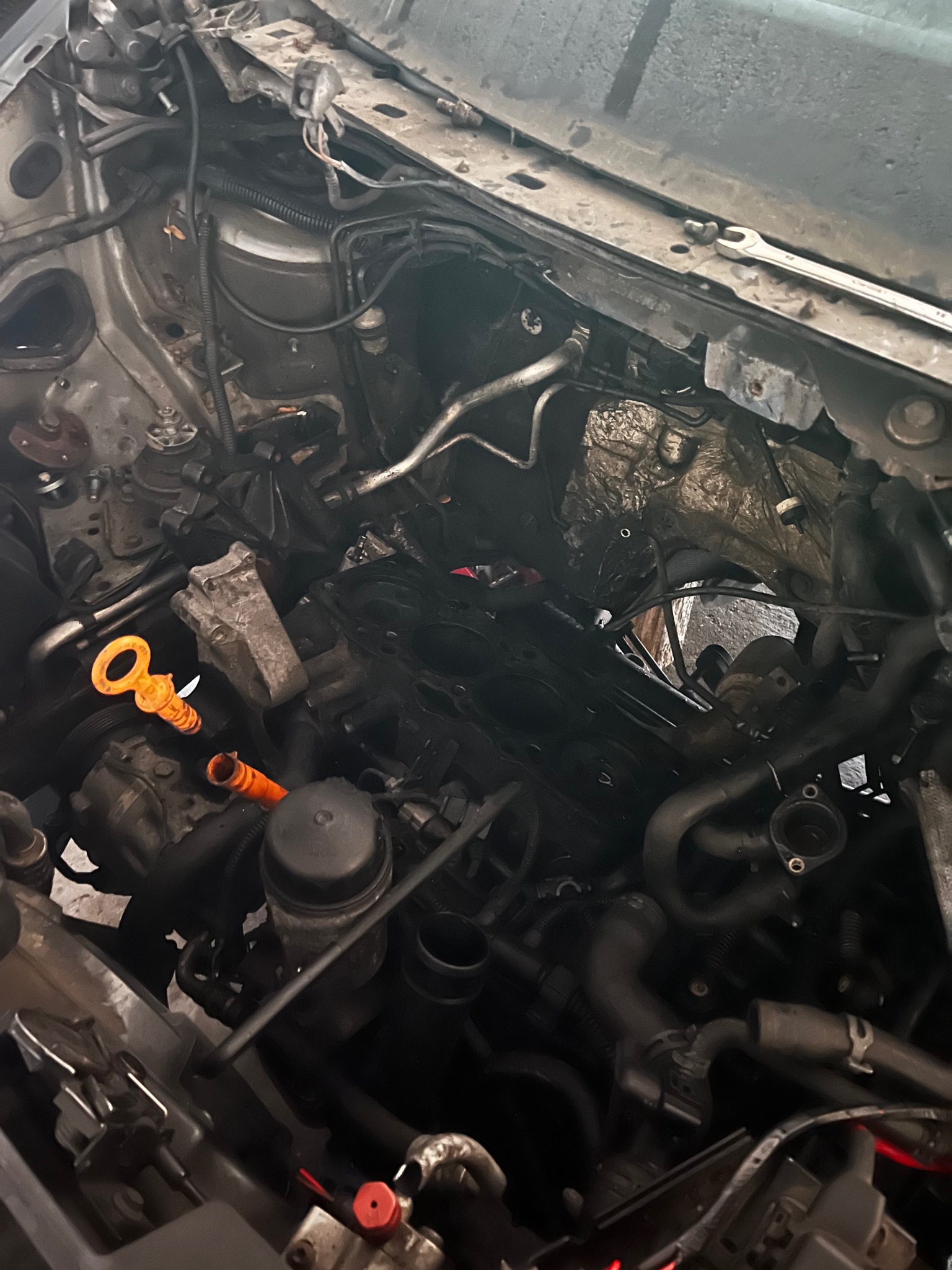 Otwarta komora silnika samochodu w trakcie naprawy, widoczne przewody, osprzęt silnika i pomarańczowy bagnet oleju.