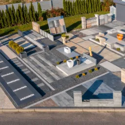 Ekspozycja różnorodnych nawierzchni z kostki brukowej i elementów betonowych na zewnątrz salonu sprzedaży, widok z góry, prezentacja aranżacji z roślinami ozdobnymi i elementami małej architektury.