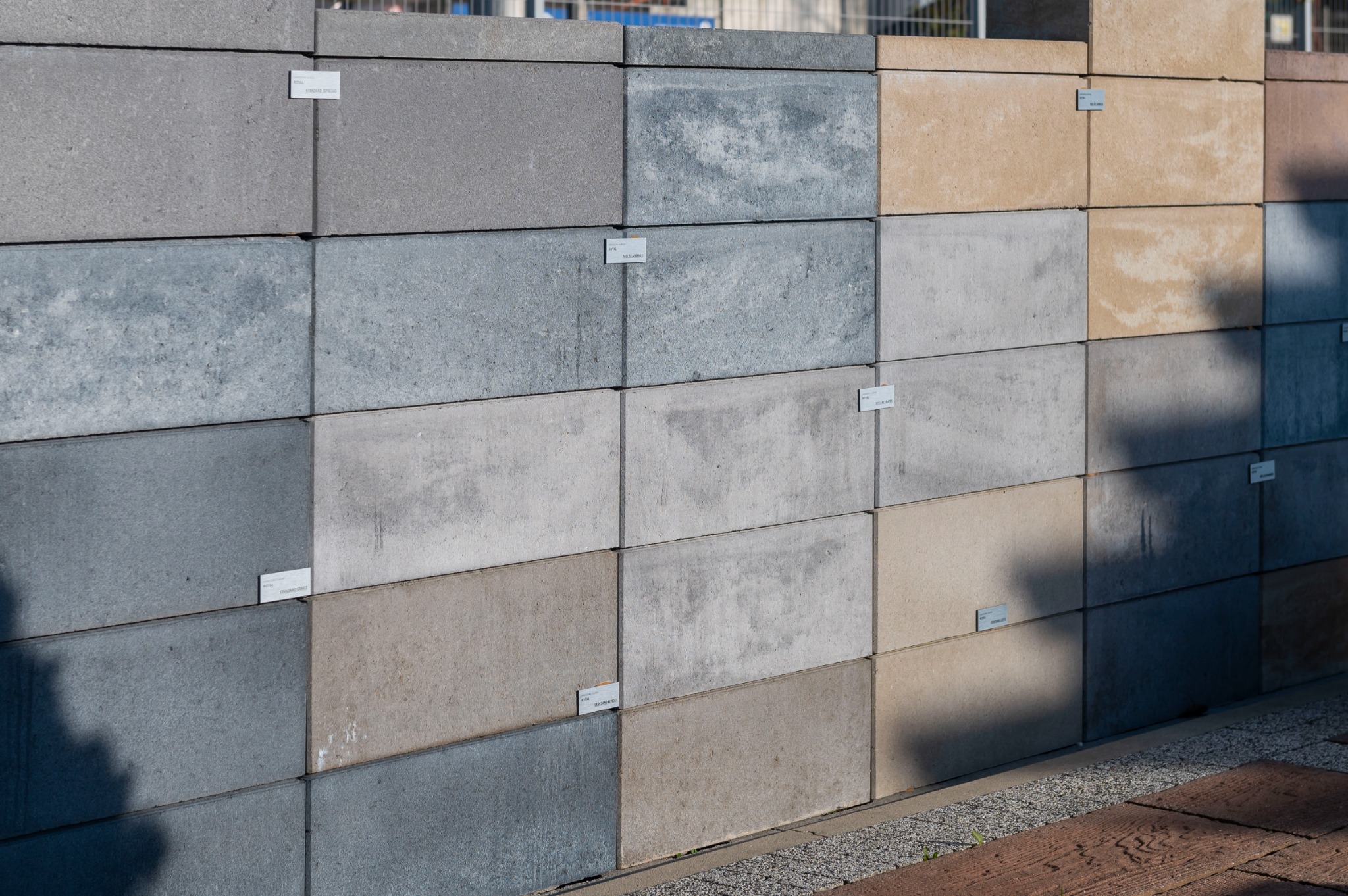 Ekspozycja różnych kolorów i faktur prostokątnych kostek betonowych z etykietami, ułożonych warstwowo, prezentujących próbki materiałów.