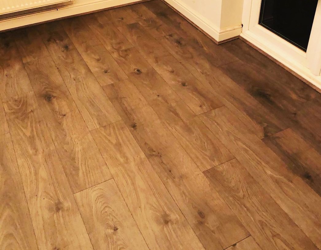 Ukończona podłoga z paneli imitujących drewno, widok z niskiego kąta, listwy przypodłogowe w kolorze złamanej bieli.