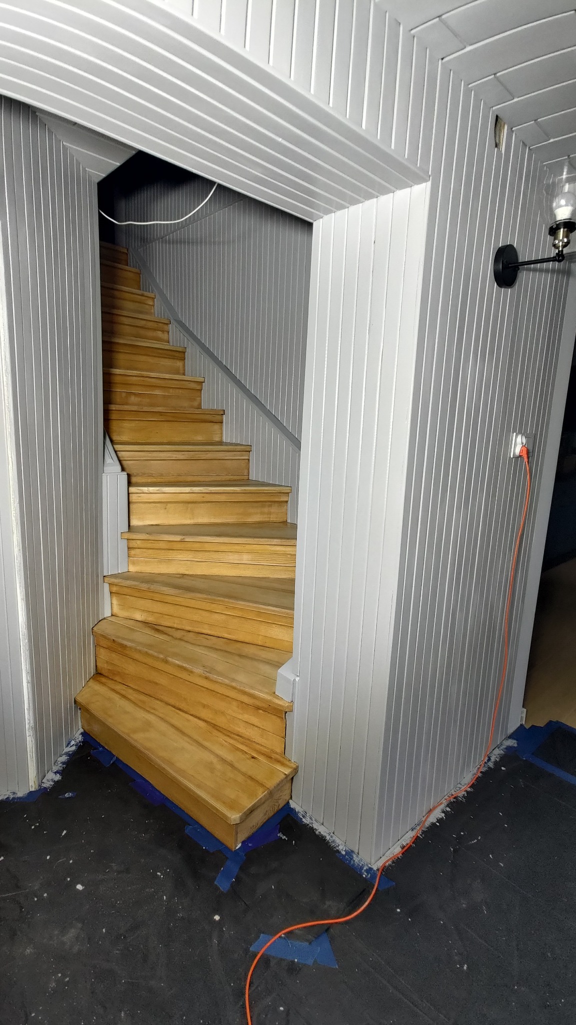 Drewniane schody z szarą balustradą w pomieszczeniu z boazerią. Widoczny kabel elektryczny i zabezpieczona podłoga. Ujęcie z dołu, podkreślające wysokość schodów.