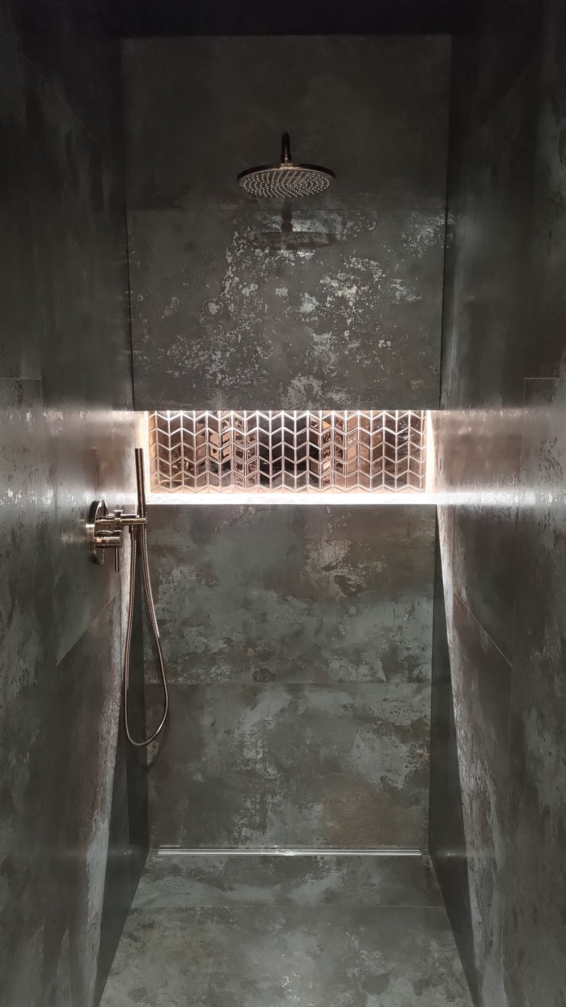 Nowoczesna kabina prysznicowa z szarymi płytkami imitującymi beton, deszczownicą i dekoracyjną wnęką z mozaiką podświetloną LED, tworząca unikalny efekt wizualny.