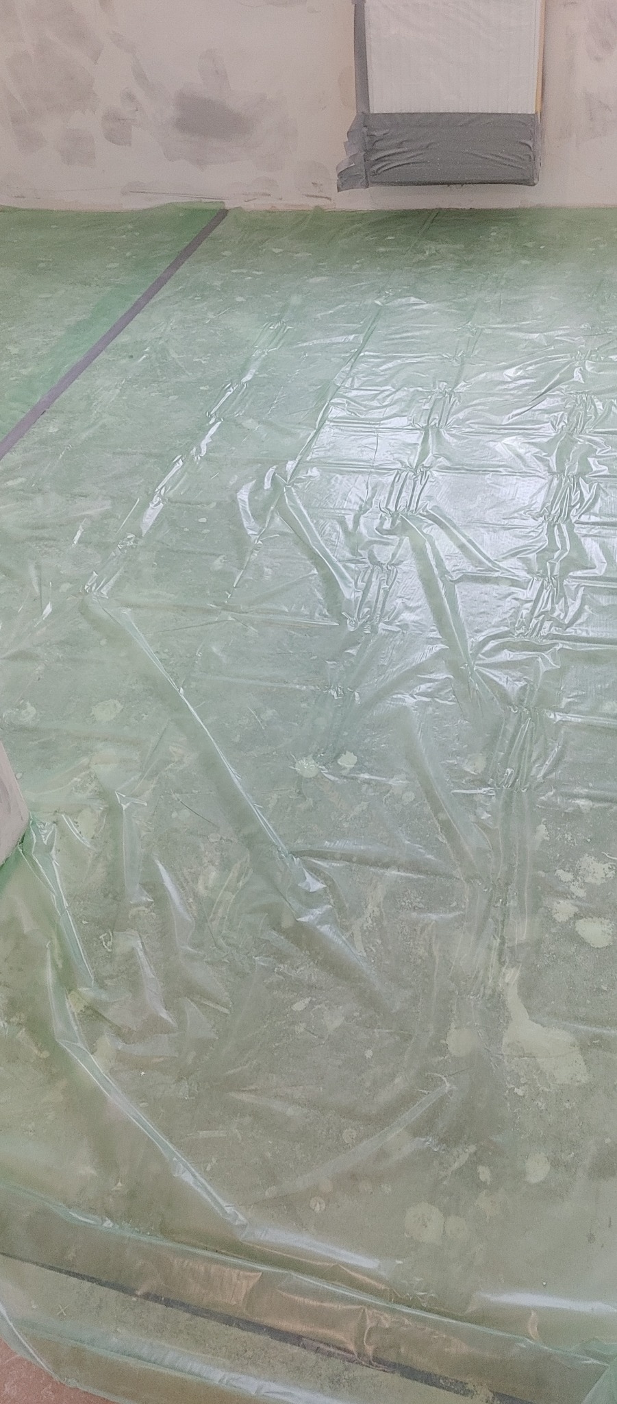 Podłoga zabezpieczona folią ochronną i taśmą malarską przed rozpoczęciem prac, widoczne ślady farby na podłodze i ścianie