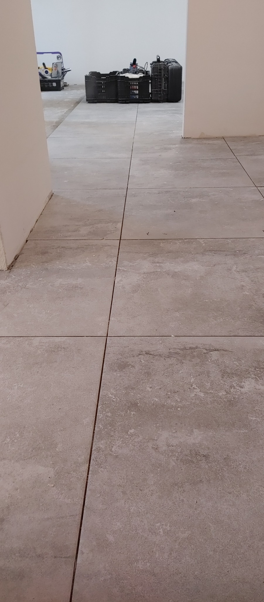 Ułożone beżowe płytki podłogowe z widocznymi fugami, w tle narzędzia i pojemniki glazurnicze