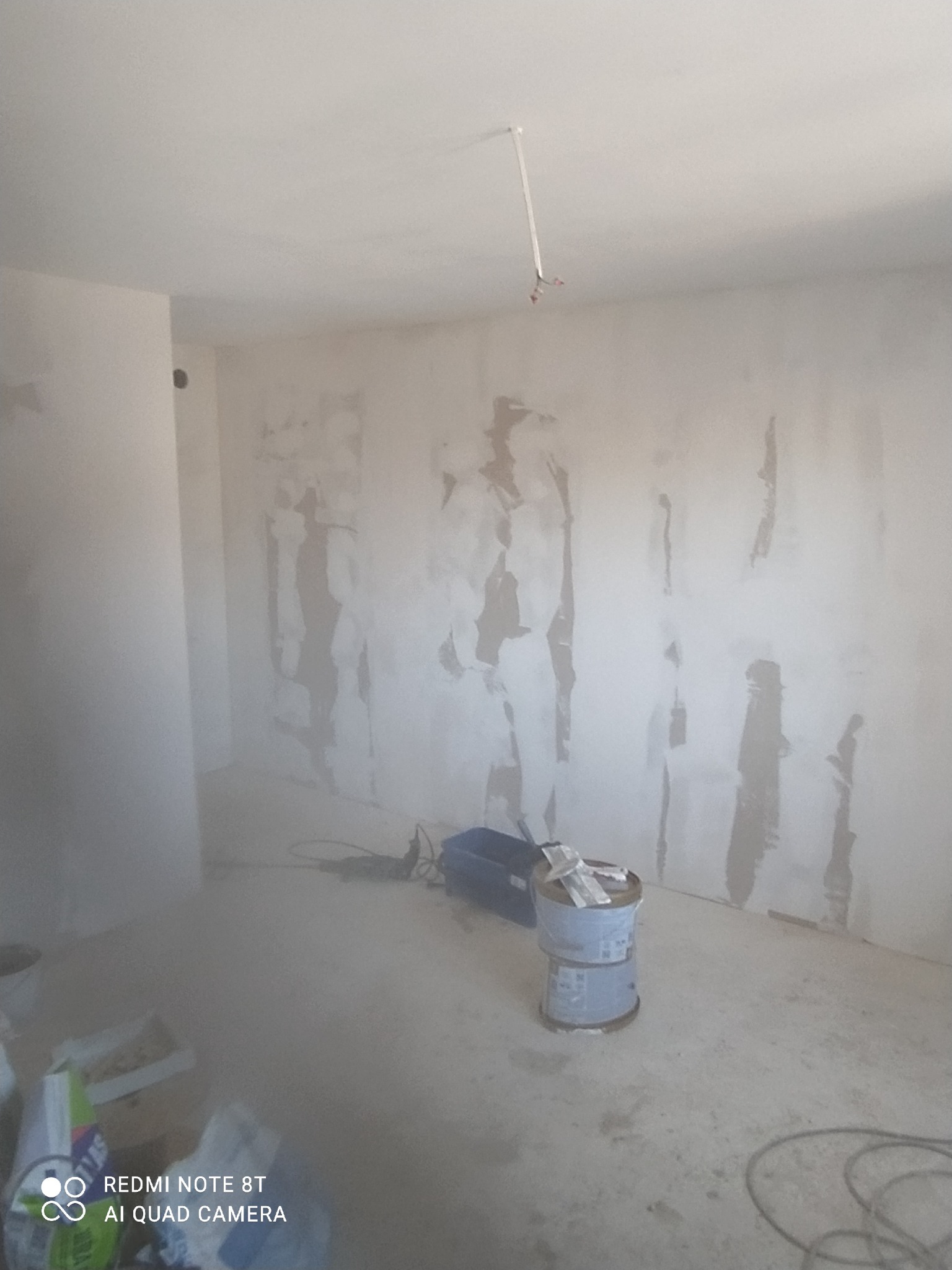 Pokój w trakcie prac wykończeniowych: ściany z widocznymi śladami szpachlowania, narzędzia i puszki z materiałami budowlanymi na podłodze.