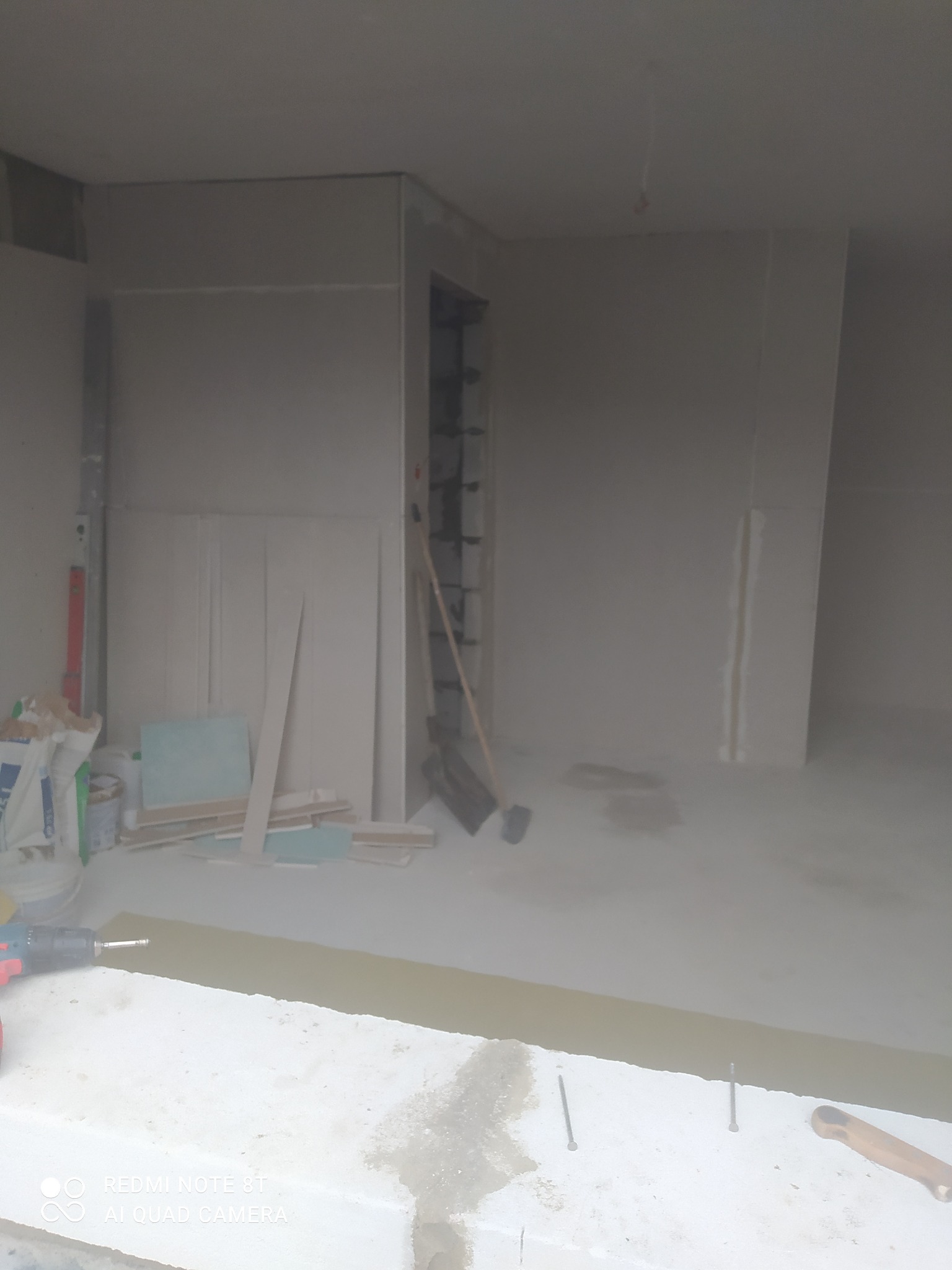 Wnętrze w trakcie prac wykończeniowych w Łabuniach: widoczne płyty gipsowo-kartonowe na ścianach, narzędzia, poziomica i wiadro z zaprawą, przygotowane do szpachlowania.