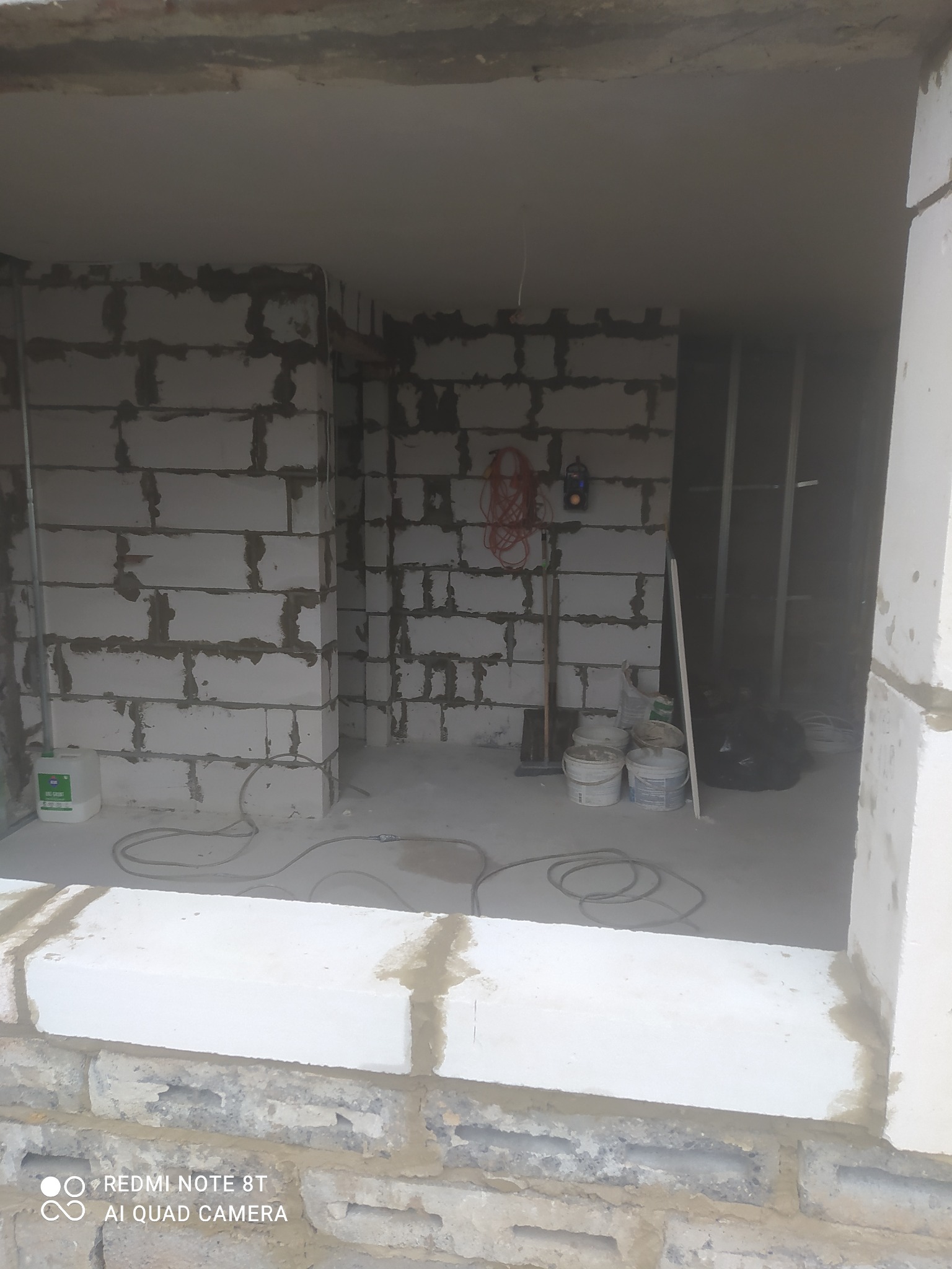 Wnętrze w trakcie remontu: ściany z bloczków, widoczne narzędzia, wiaderka z farbą i przewody elektryczne, surowy stan wykończenia.