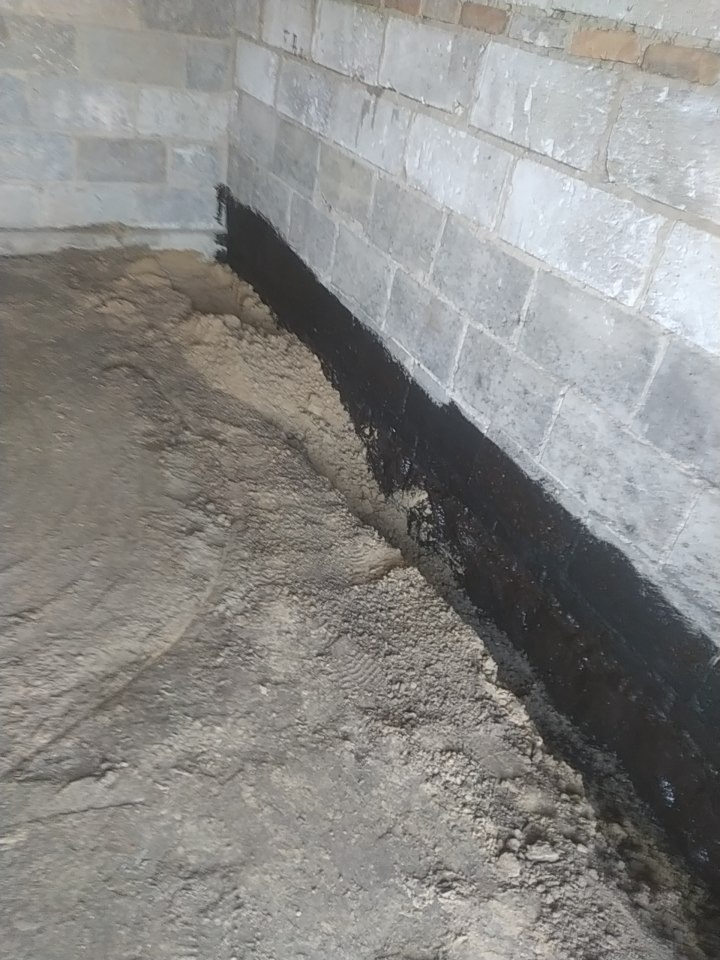 Blok betonowy fundamentu z nałożoną grubą warstwą czarnego uszczelnienia przeciwwilgociowego na styku z podłożem.