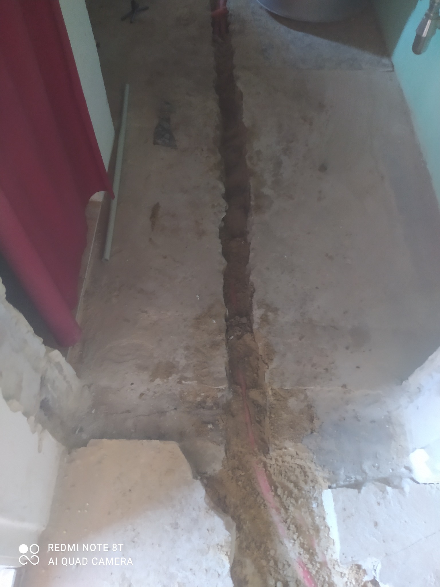 Wykopana bruzda w betonowej podłodze z widoczną rurką instalacyjną, przygotowana do zalania zaprawą.