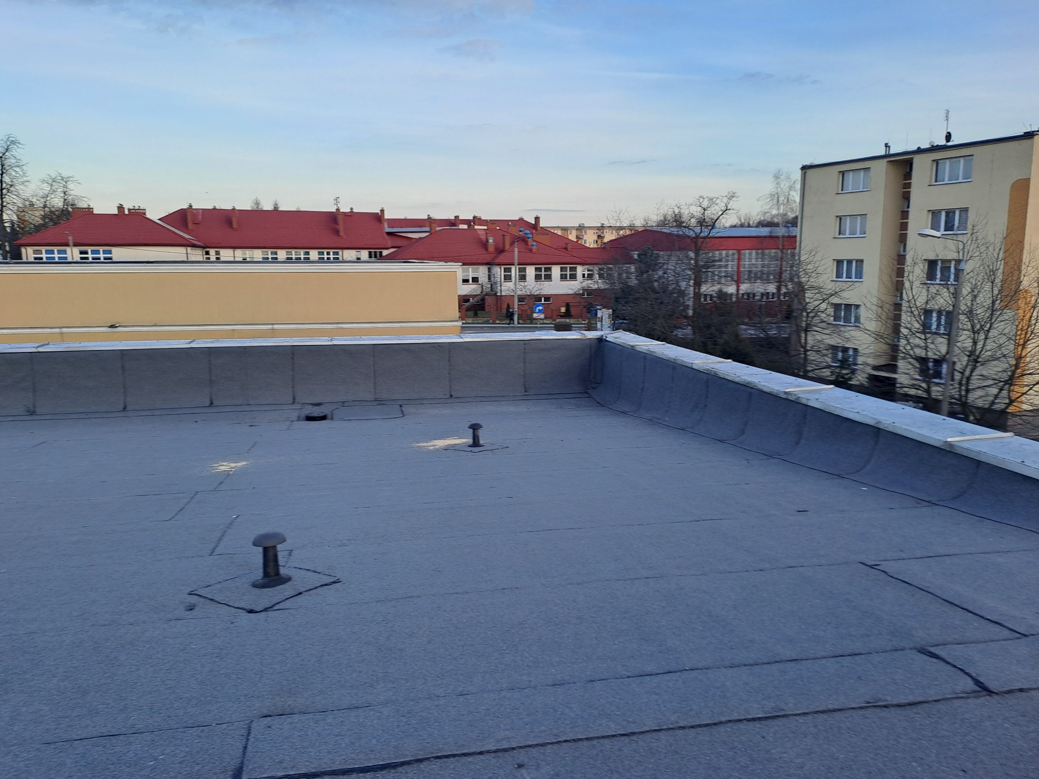Płaski dach pokryty papą termozgrzewalną z trzema kominkami wentylacyjnymi na tle zabudowy miejskiej.