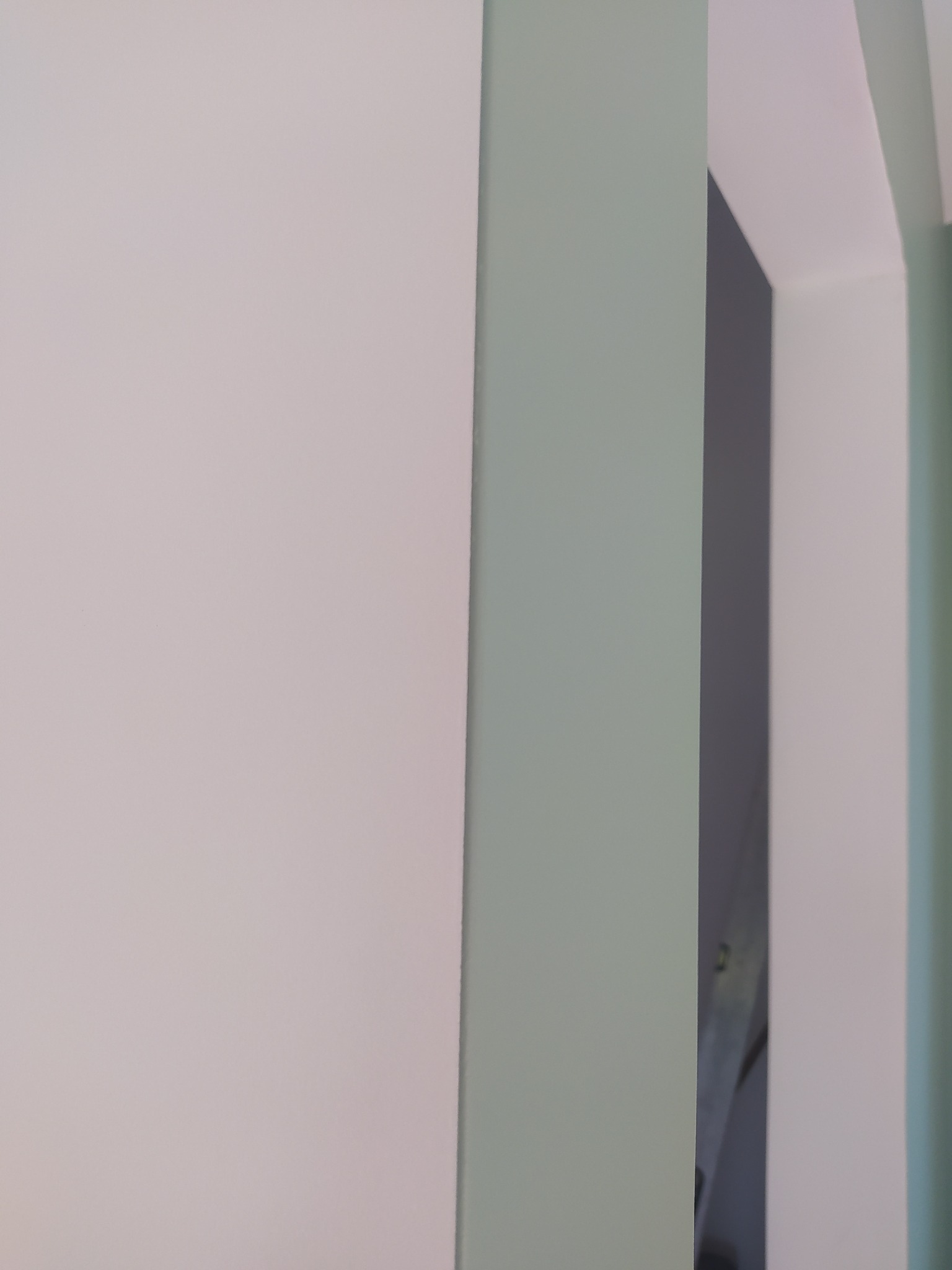 Fragment pomalowanej ściany w odcieniach bieli, szarości i zieleni, widoczny narożnik pomieszczenia i fragment sufitu.