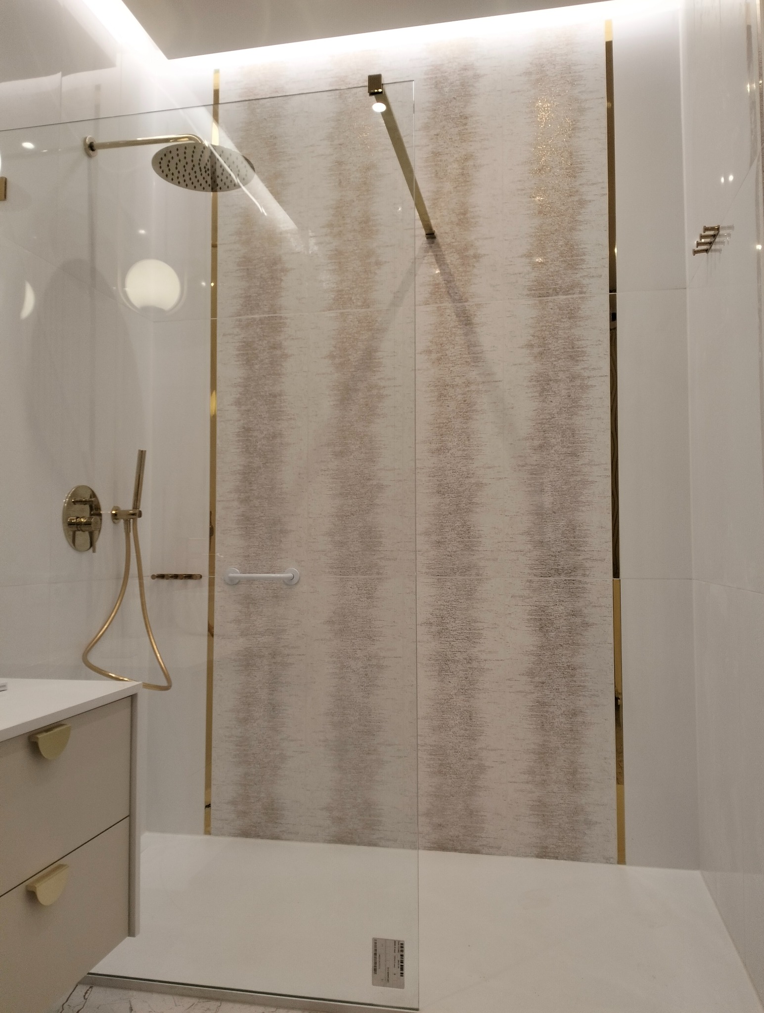 Nowoczesna kabina prysznicowa z deszczownicą i złotymi akcentami, wykończona białymi i beżowymi płytkami z subtelnym wzorem.