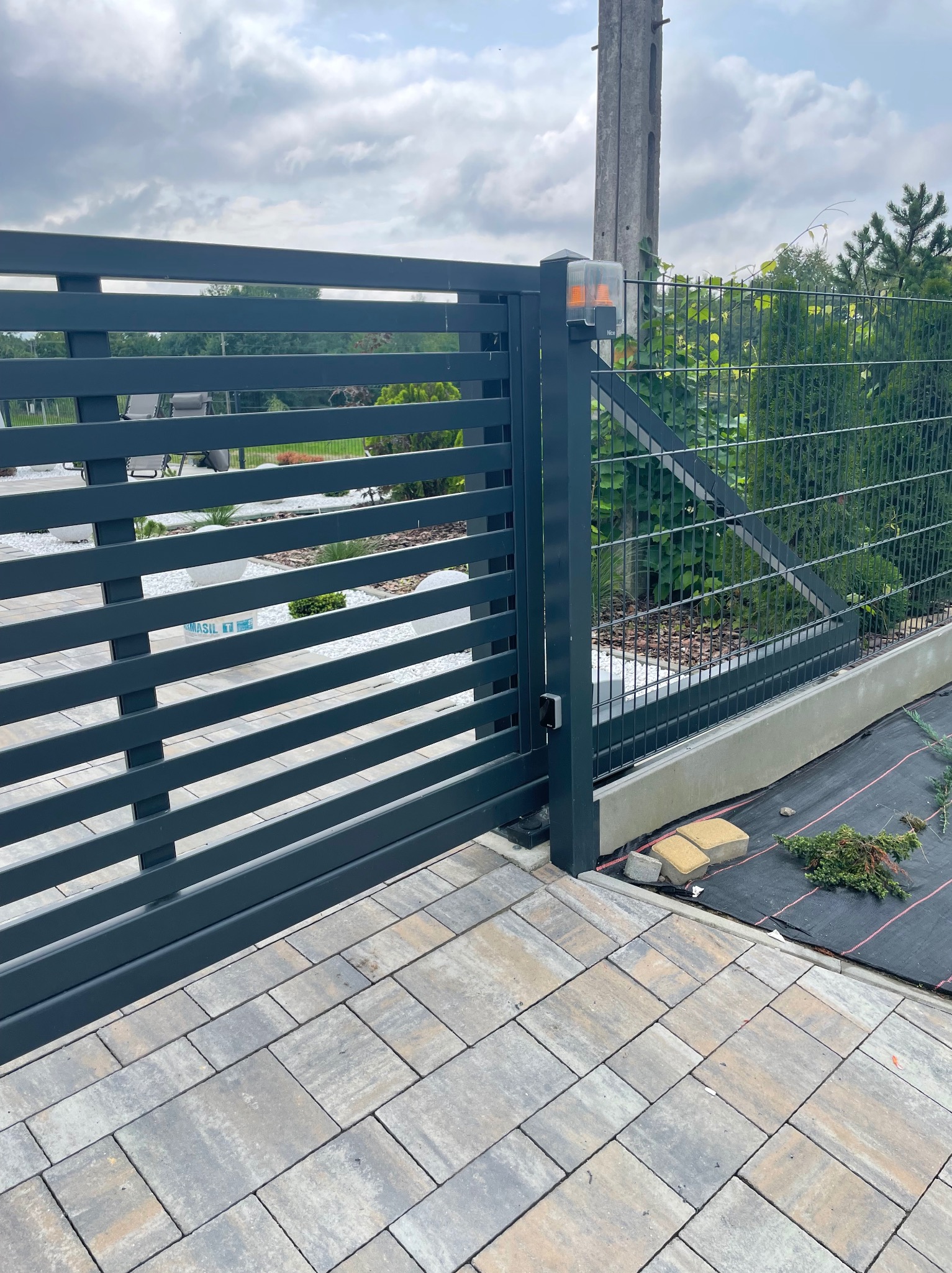 Nowoczesna, pozioma brama wjazdowa z automatyką i lampą ostrzegawczą, zainstalowana w Kamionnej, z widocznym fragmentem posesji i kostką brukową.