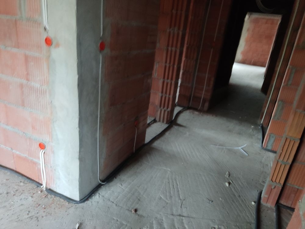 Wnętrze w trakcie prac wykończeniowych: widoczne przewody elektryczne prowadzone wzdłuż ściany z cegły, osadzone w peszlu, z przygotowanymi punktami pod gniazdka.