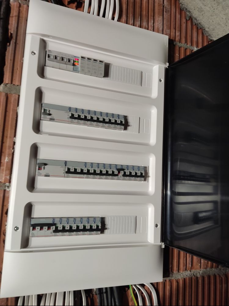 Otwarta skrzynka rozdzielcza z widocznymi bezpiecznikami i przewodami na tle ceglanej ściany.