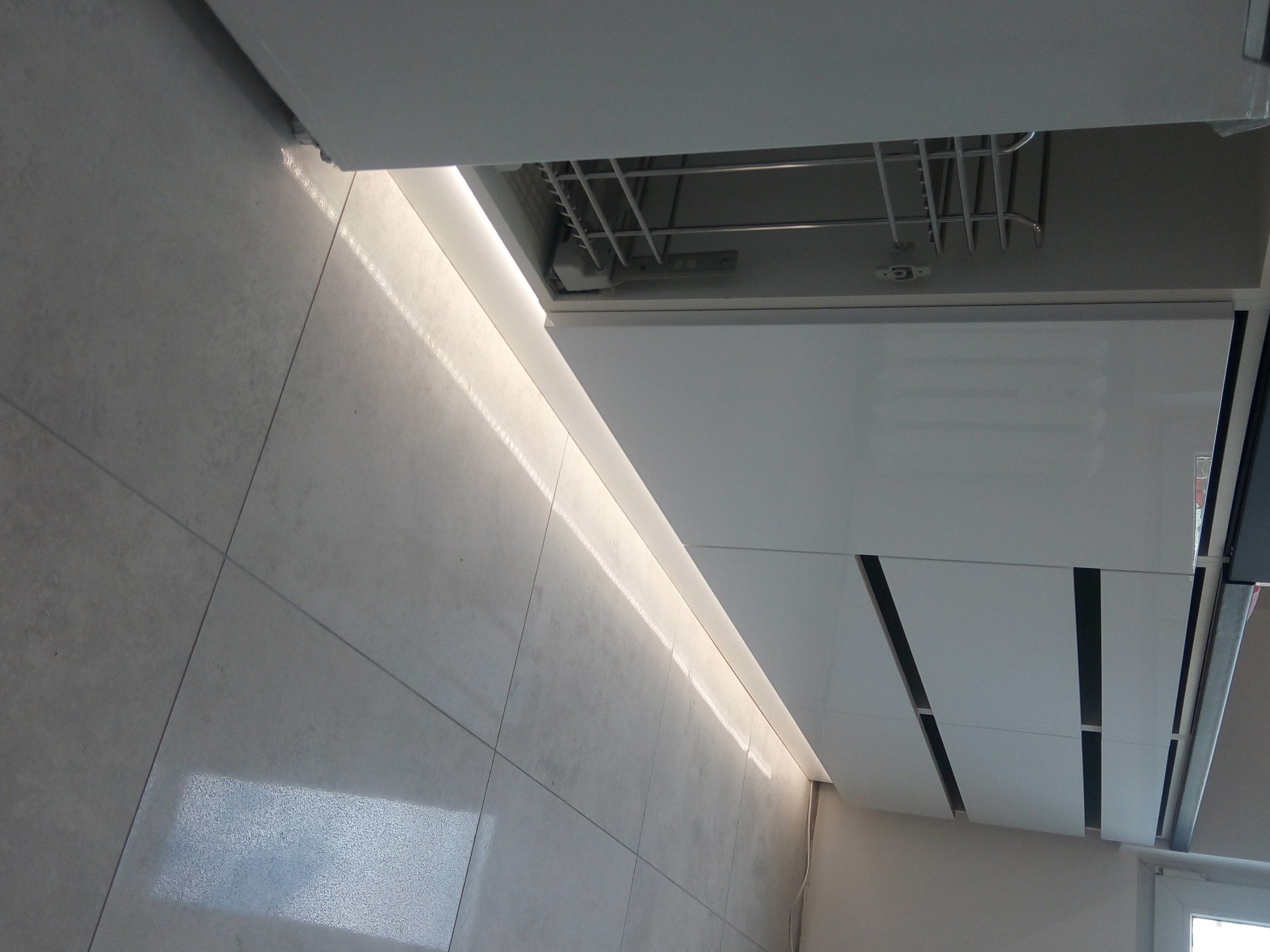 Nowoczesna, biała zabudowa kuchenna z podświetleniem LED podszafkowym, widok na szuflady i fragment podłogi z płytek.