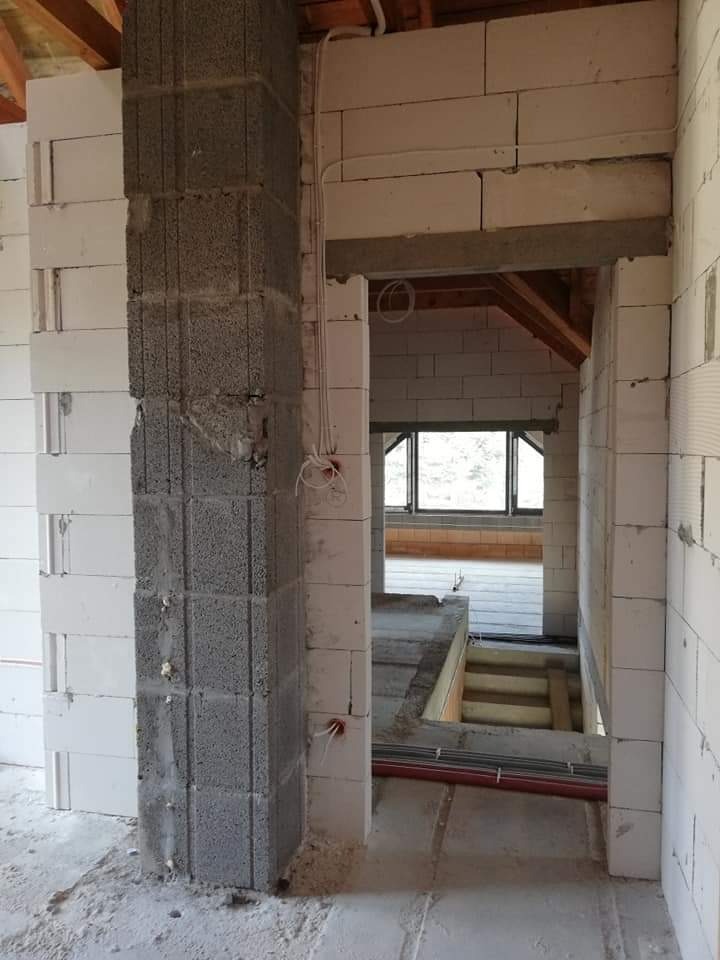 Surowy stan instalacji elektrycznej w nowo budowanym domu z widocznymi przewodami i puszkami w ścianach z betonu komórkowego, filar częściowo otynkowany.