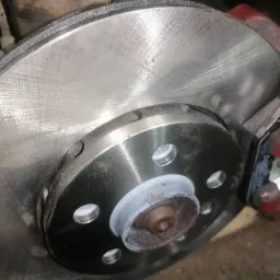 Nowa tarcza hamulcowa zamontowana na piaście, widoczny zacisk hamulcowy pomalowany na czerwono, detale montażu.