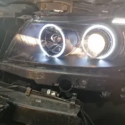 Reflektor samochodowy z ringami LED, widoczne elementy demontażu i instalacji, zbliżenie na przedni fragment pojazdu.