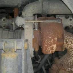 PG Mechanika & Elektronika Samochodowa - Zardzewiała turbosprężarka w samochodzie, widoczna od spodu, z elementami układu wydechowego i zawieszenia. Widoczne ślady korozji i zużycia.