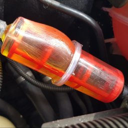 PG Mechanika & Elektronika Samochodowa - Przezroczysty filtr paliwa z pomarańczowo-czerwonym wkładem, zamontowany w przewodzie paliwowym silnika w Pomiechówku, zabezpieczony opaskami zaciskowymi.