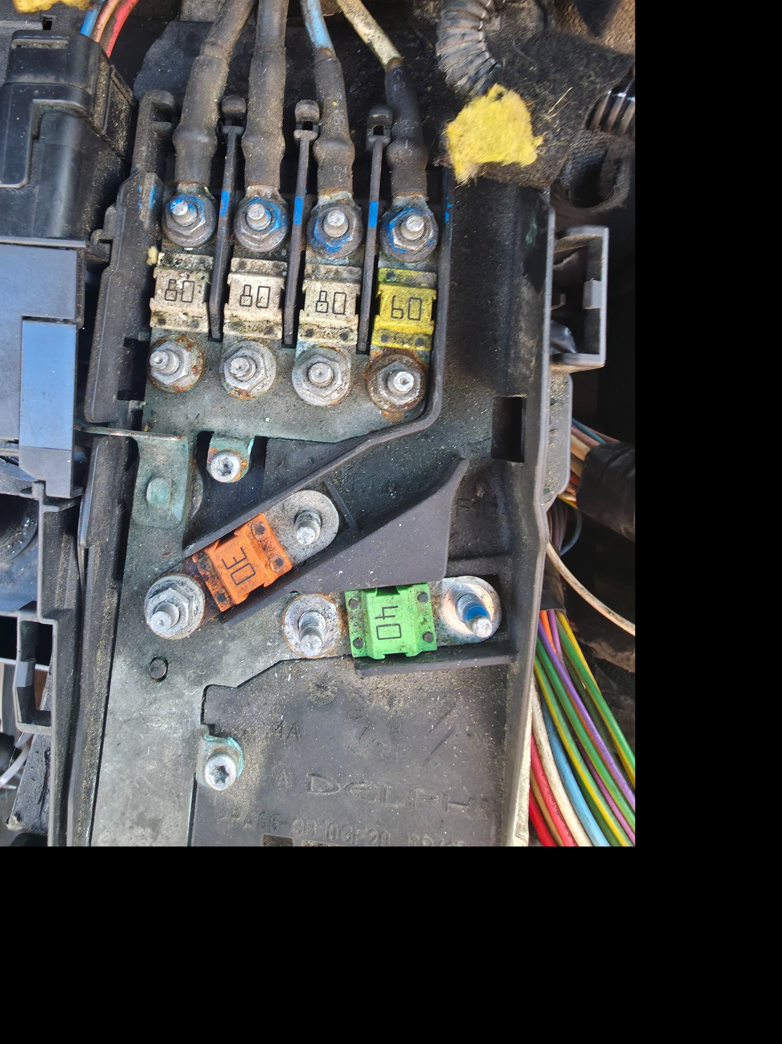 Skrzynka bezpieczników samochodowych z widocznymi bezpiecznikami o różnych amperażach i przewodami. Widoczne ślady użytkowania i potencjalne korozji.