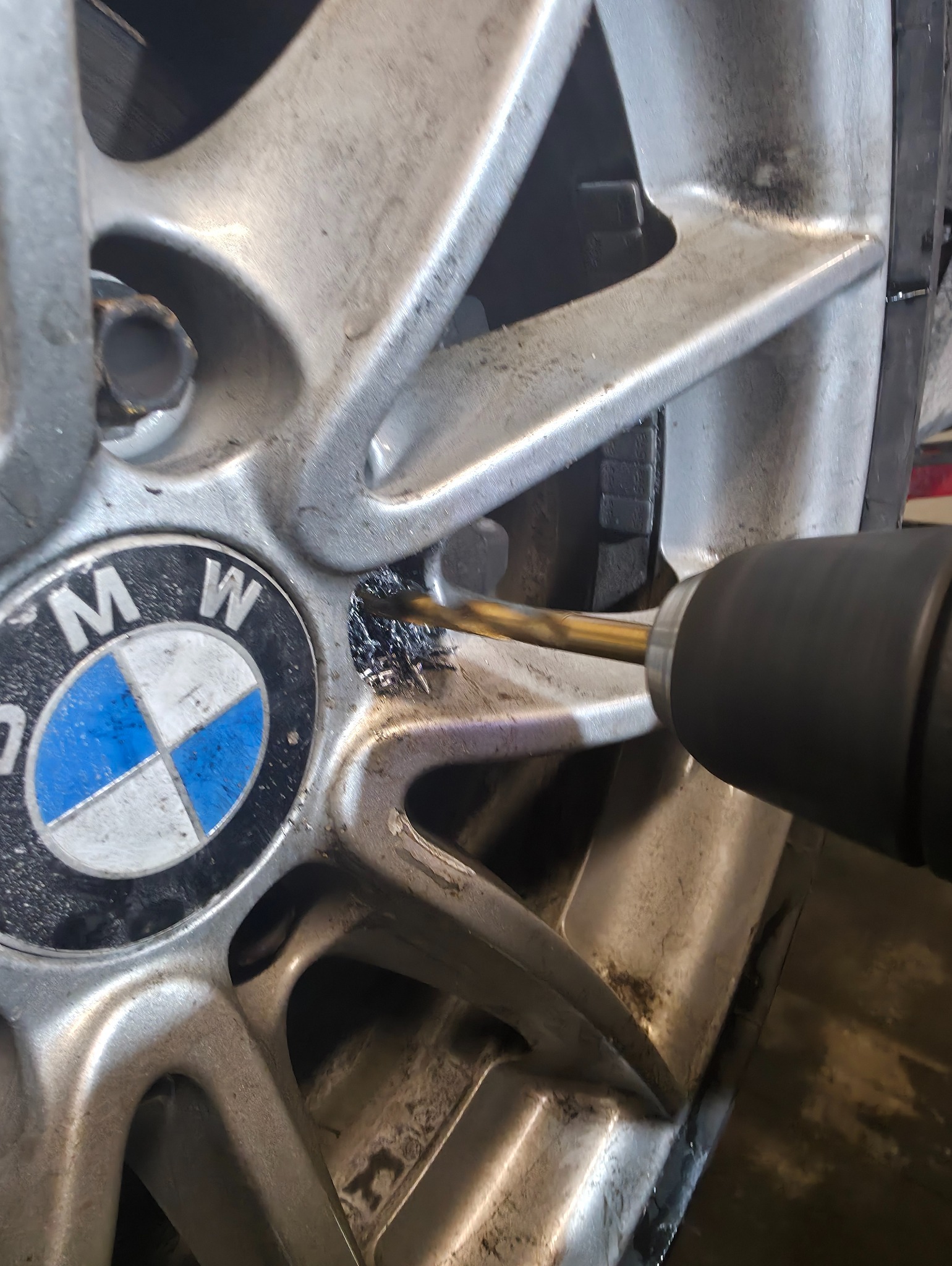 Wiertarka obok felgi BMW, w trakcie wiercenia. Widoczne opiłki metalu. Obróbka felgi aluminiowej w warsztacie.