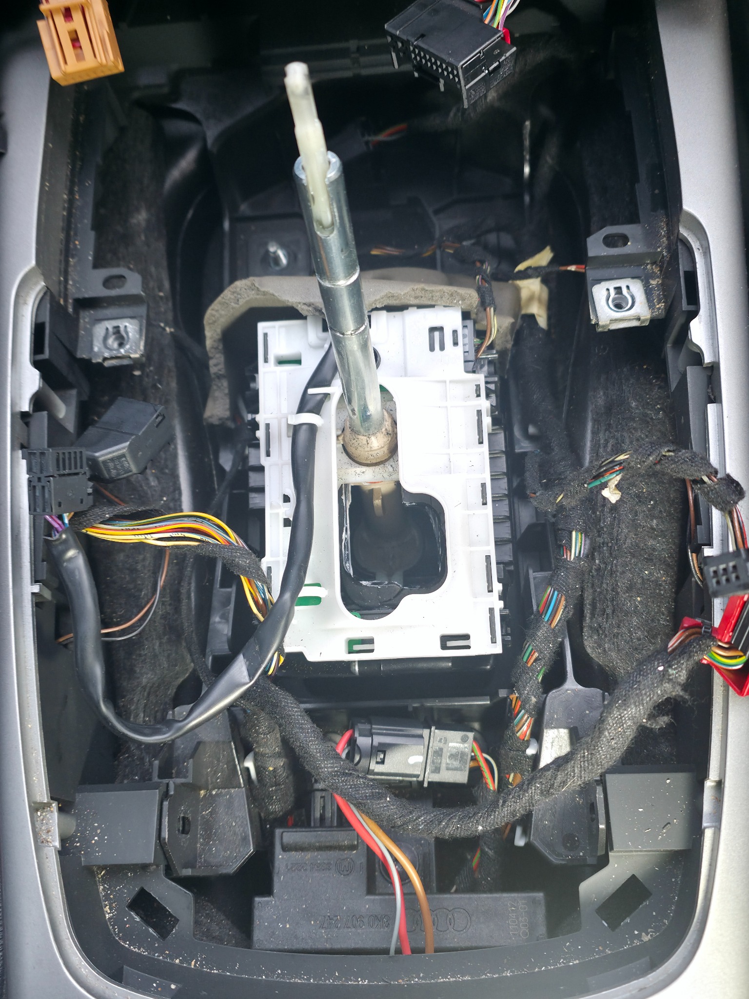 Wnętrze samochodu z widocznym mechanizmem zmiany biegów w trakcie naprawy. Widoczne przewody i elementy konstrukcyjne.