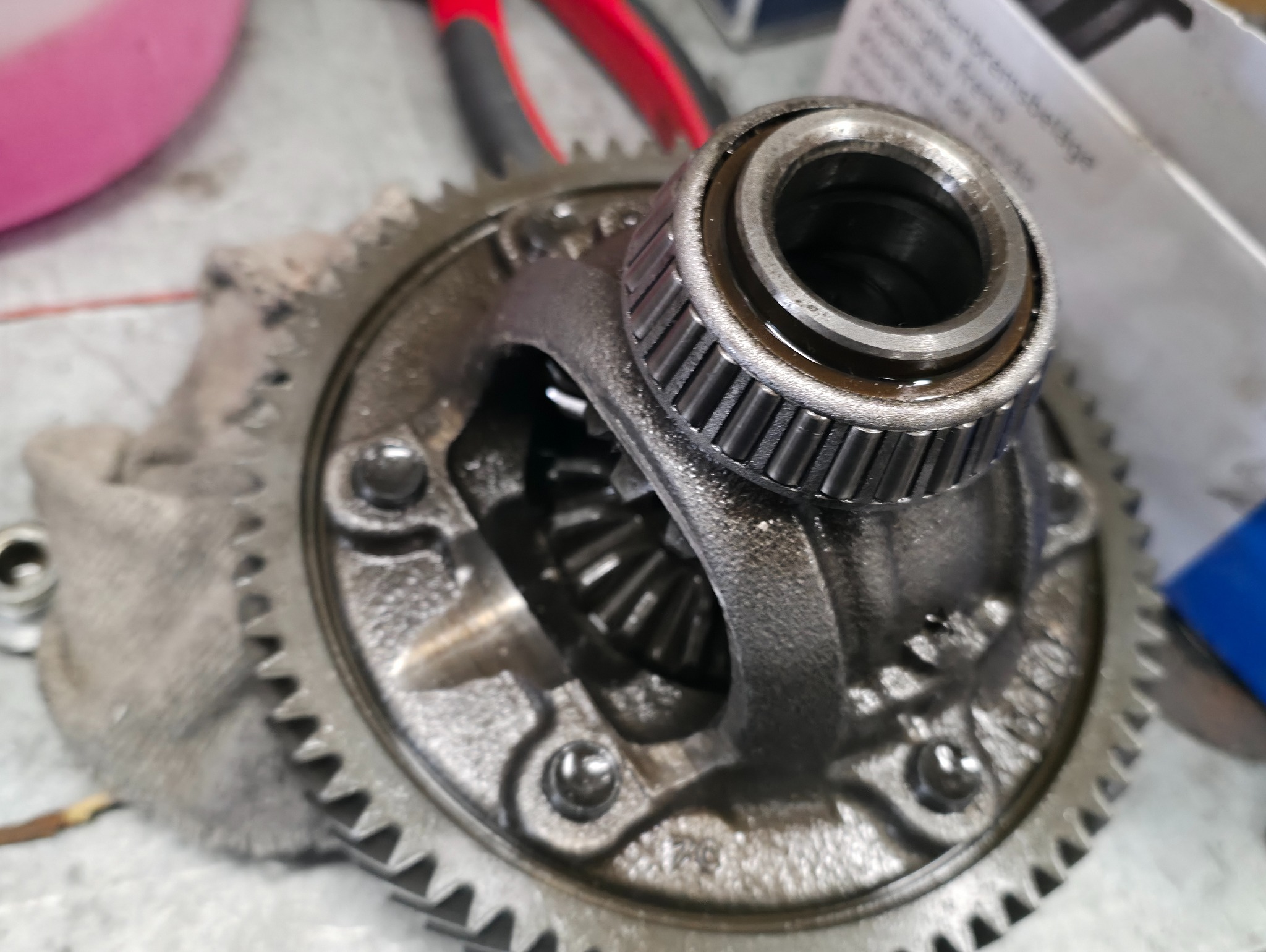 Metalowa przekładnia z łożyskiem stożkowym w zbliżeniu, widoczne ślady oleju i zabrudzenia, sugerujące etap naprawy lub konserwacji w warsztacie samochodowym.