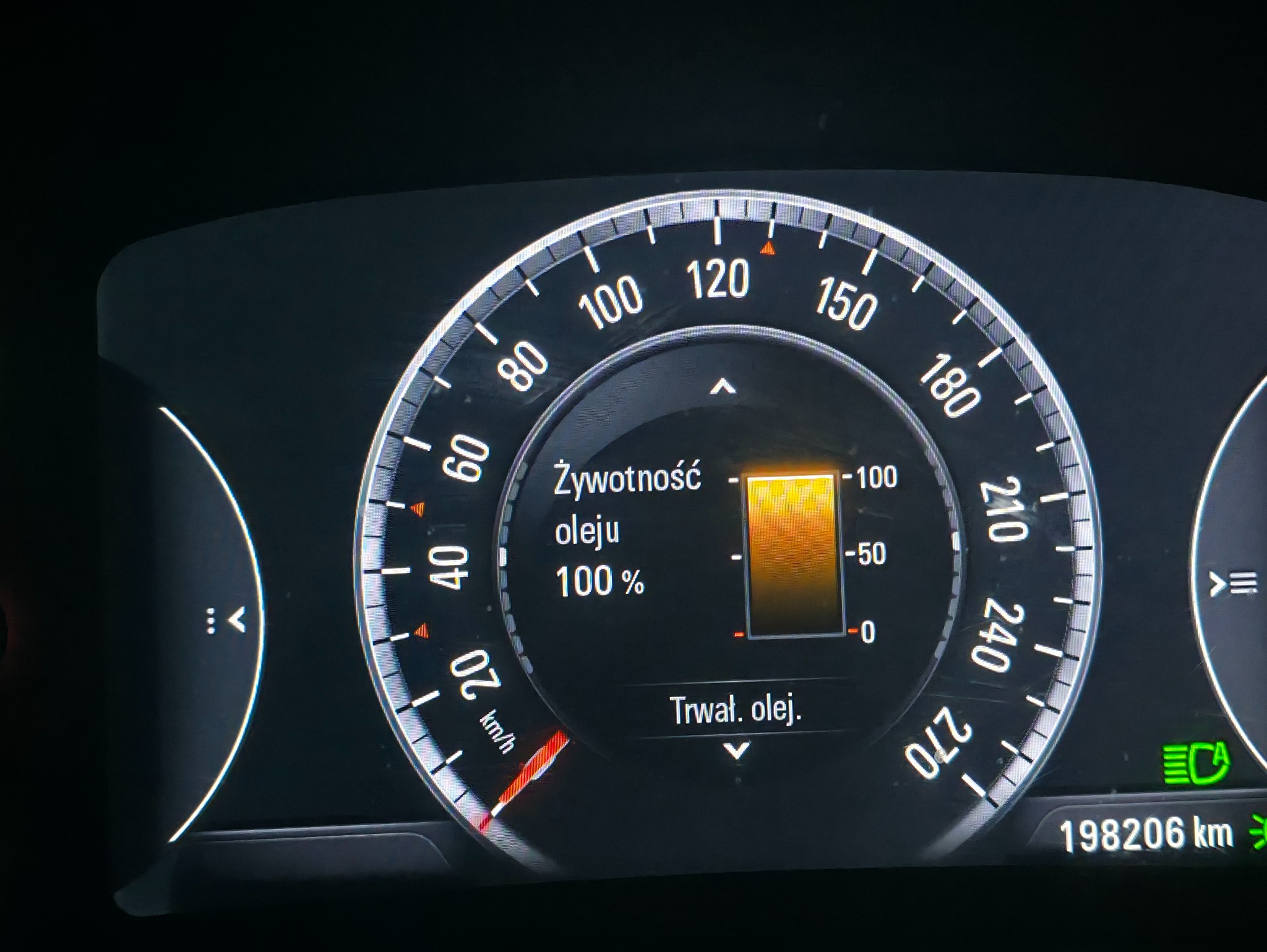 Deska rozdzielcza samochodu z wyświetlonym wskazaniem 100% żywotności oleju. Widoczny przebieg pojazdu. Ujęcie z bliska, ciemne tło.