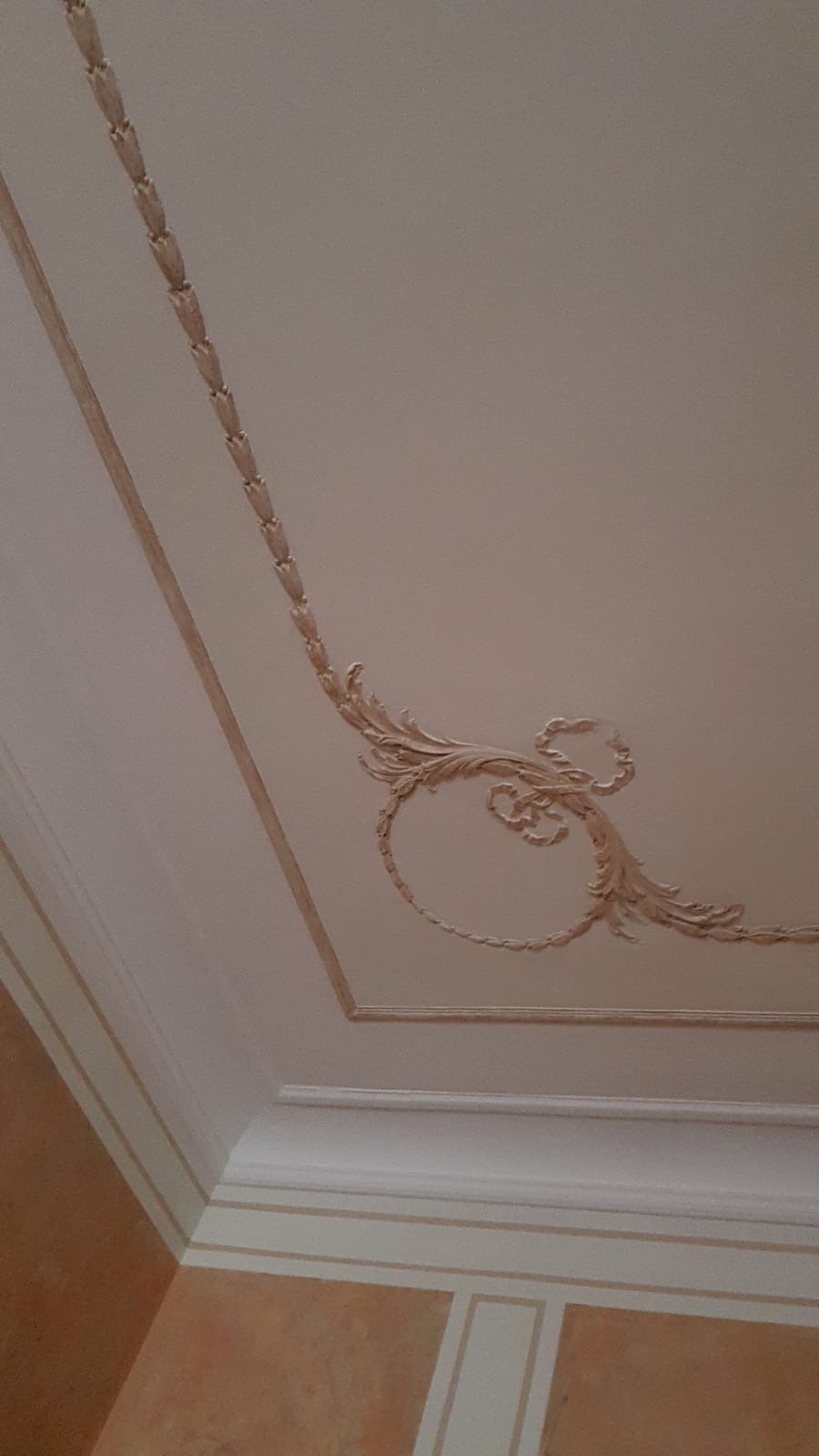 Dekoracyjny sufit z gładzią i ornamentami w stylu klasycznym, wykończony listwami i delikatnymi zdobieniami.