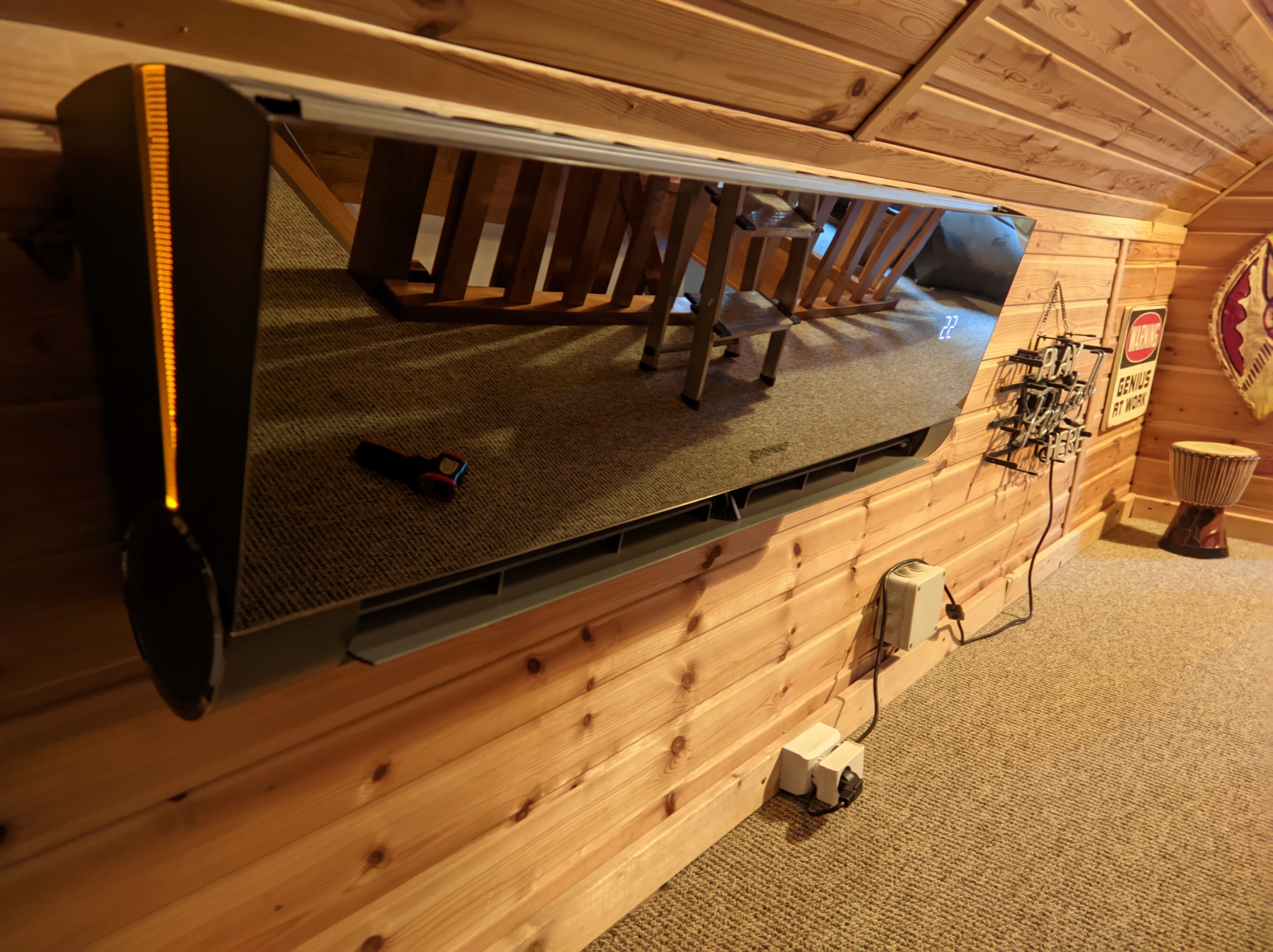 Nowoczesny klimatyzator ścienny w drewnianym wnętrzu poddasza, z widocznym wyświetlaczem temperatury i elementami dekoracyjnymi na ścianie.