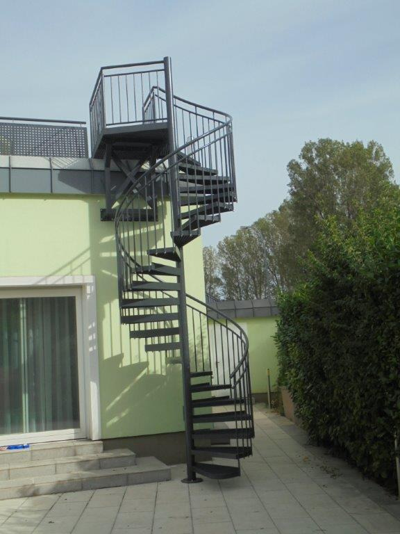 Zewnętrzne, metalowe schody spiralne prowadzące na balkon w Szczecinie, z widoczną konstrukcją wsporczą i poręczą zabezpieczającą.