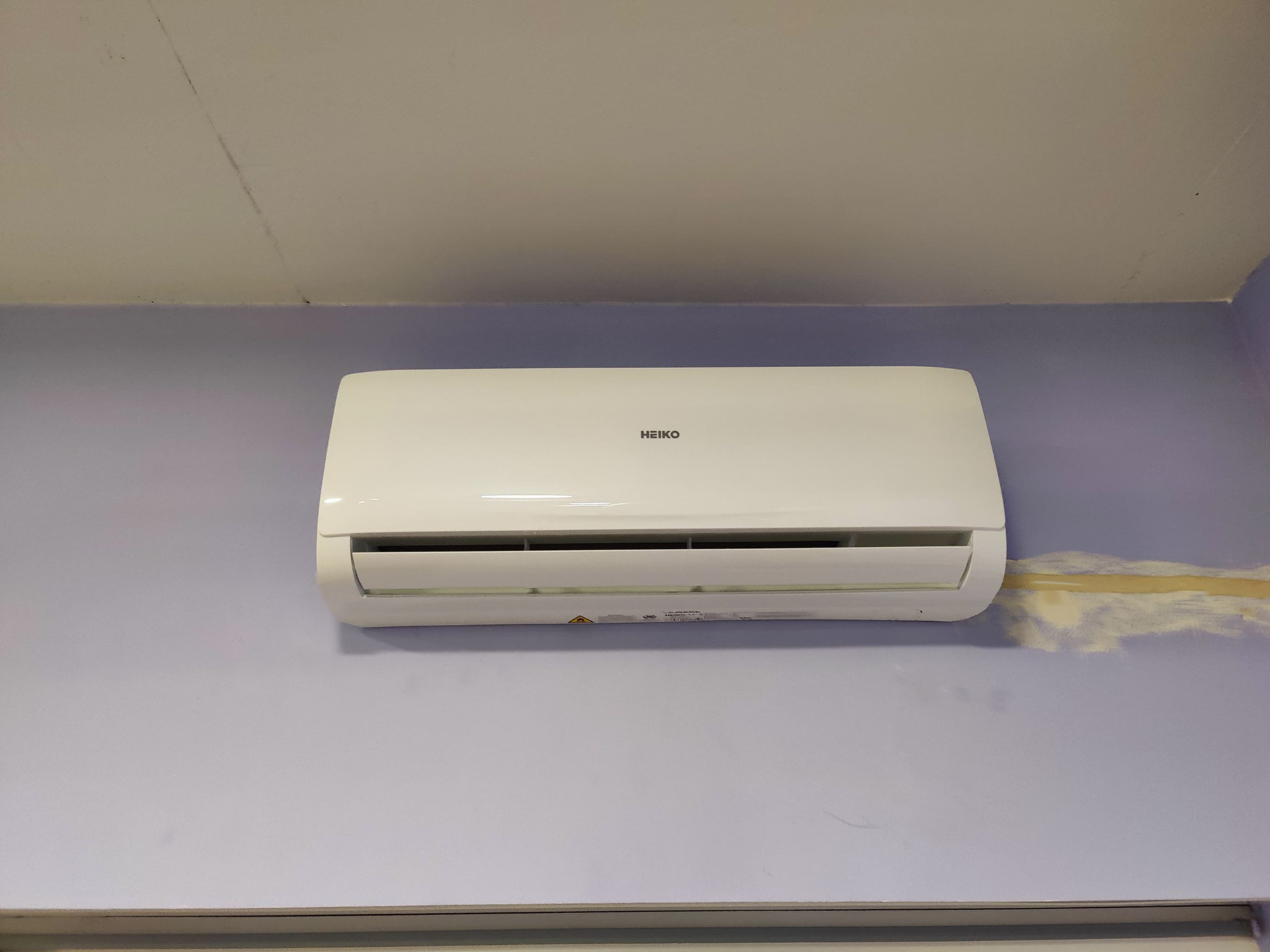 Biały klimatyzator marki HEIKO zamontowany na fioletowej ścianie w pomieszczeniu, widoczne ślady po niedawnym malowaniu wokół urządzenia.