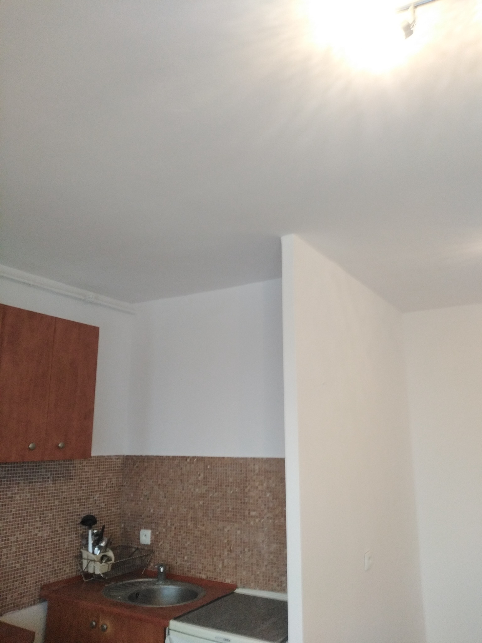 Wnętrze kuchni po remoncie: białe ściany i sufit, brązowe szafki, mozaika na ścianie nad blatem, widoczny zlew i fragment sprzętu AGD.