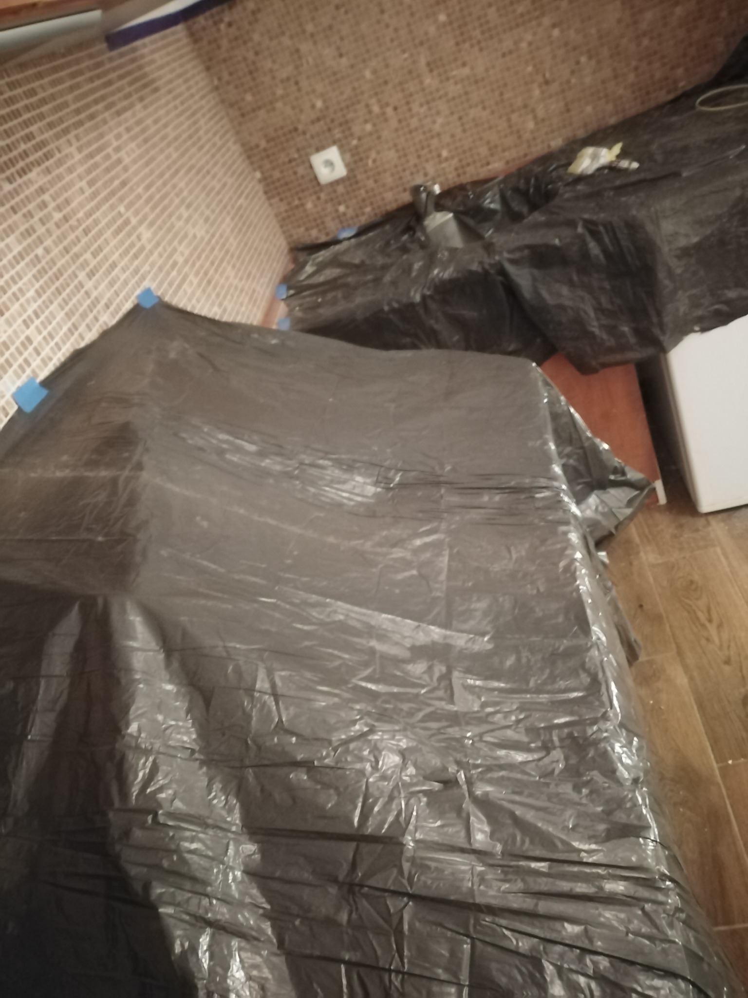 Pokój zabezpieczony folią malarską przed zabrudzeniem, widoczne płytki na ścianie i drewniana podłoga.