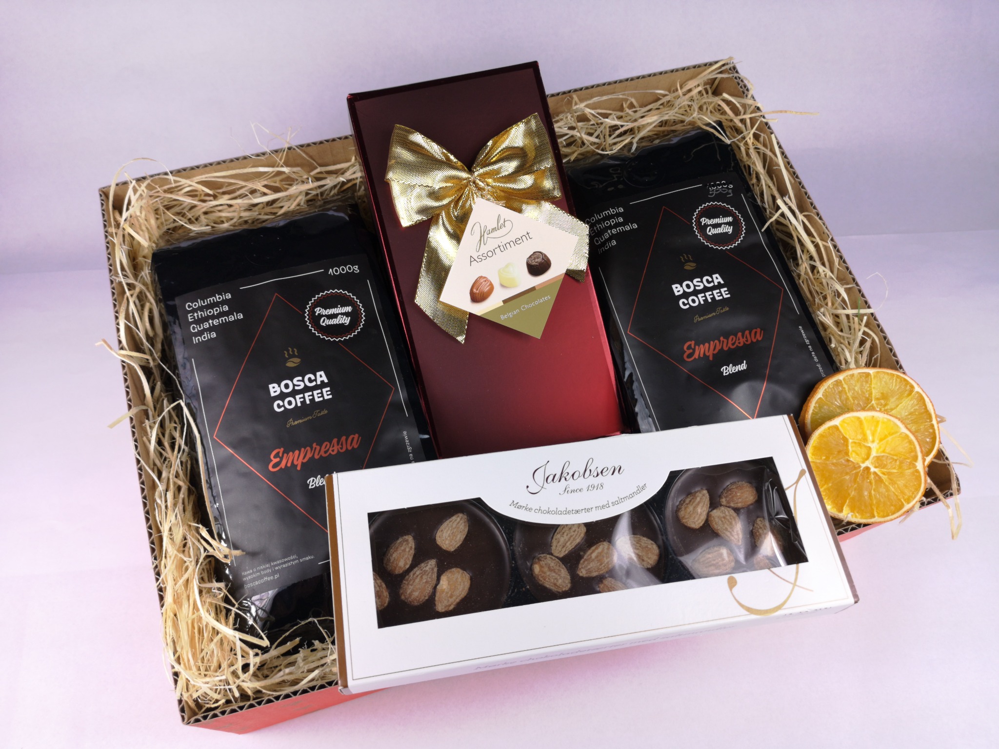 Zestaw prezentowy: dwie paczki kawy Bosca Coffee Empress Blend, pudełko czekoladek Hamlet Assortment z kokardą i pudełko Jakobsen z ciemnymi czekoladkami z migdałami, całość w koszyku z tektury...