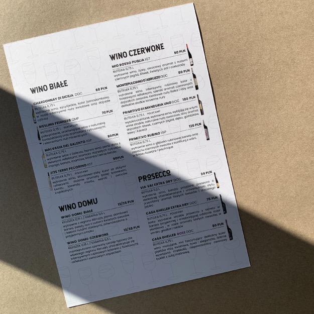 Menu restauracji z ofertą win białych, czerwonych i prosecco, z cenami i opisami, oświetlone naturalnym światłem.
