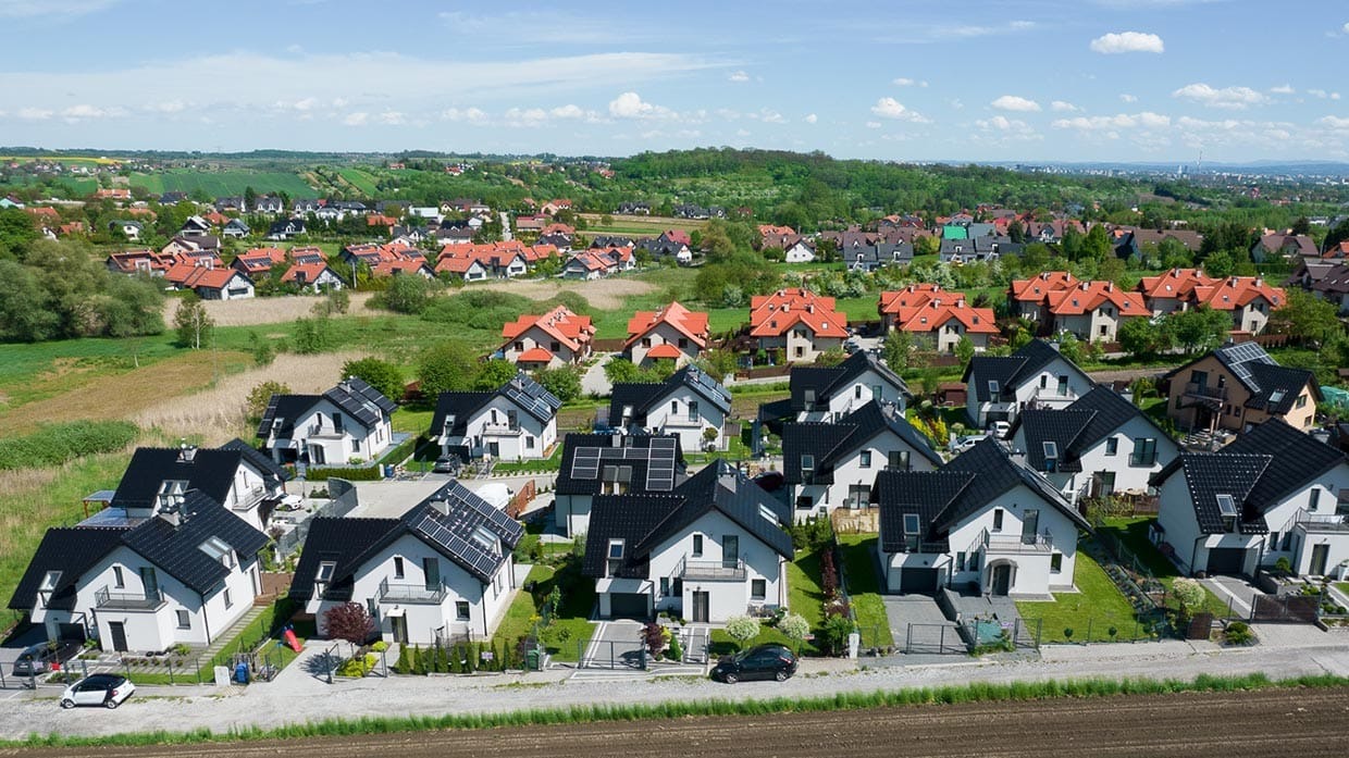 Panorama osiedla domów jednorodzinnych z panelami słonecznymi na dachach, widok z lotu ptaka w słoneczny dzień.