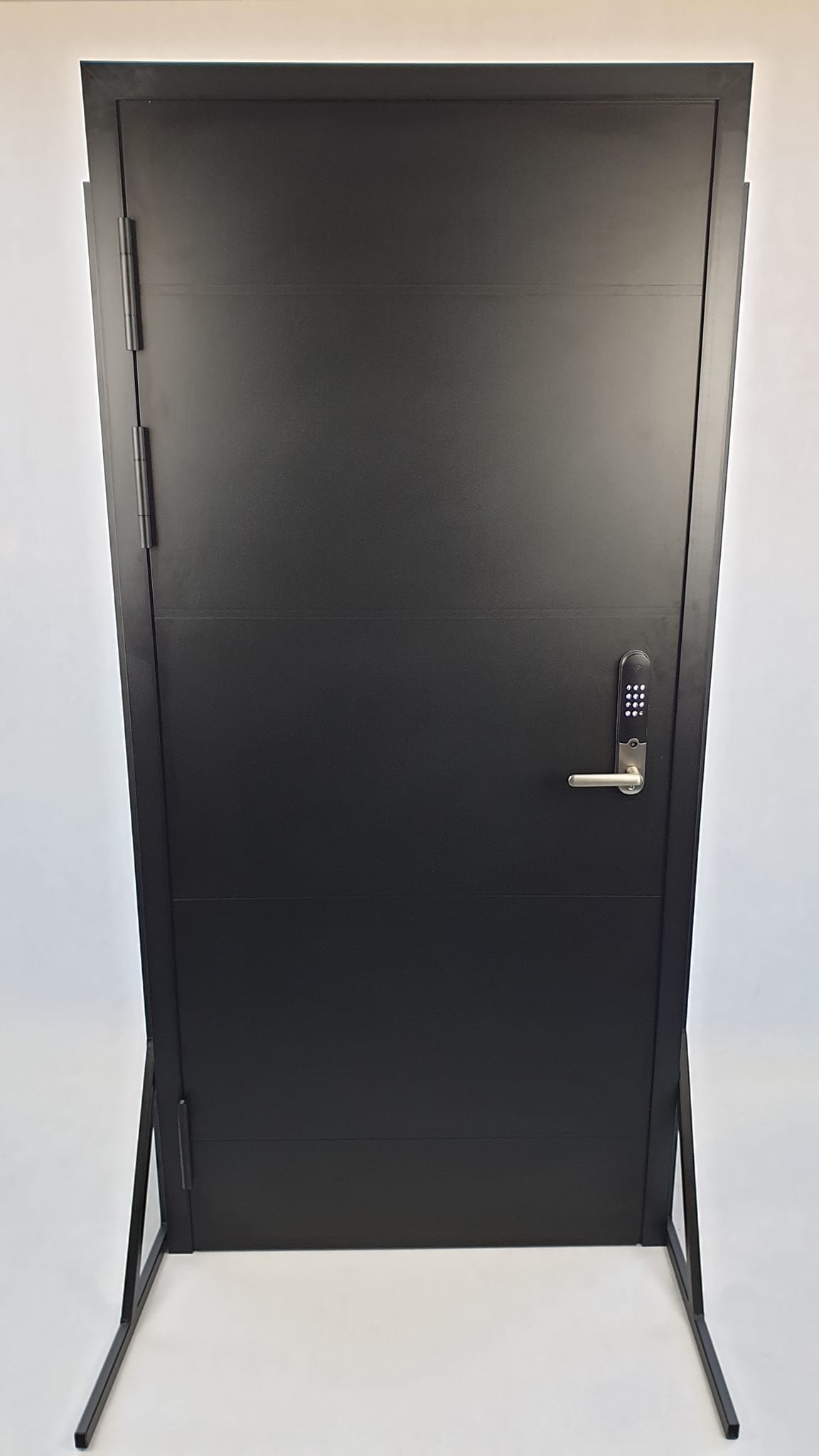 Czarne, stalowe skrzydło z elektronicznym zamkiem na białym tle, ustawione na metalowym stojaku ekspozycyjnym.