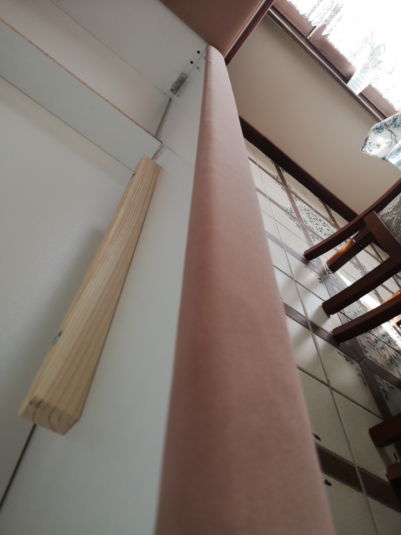 Przygotowanie do montażu tapicerowanego wezgłowia łóżka: drewniany stelaż przytwierdzony do ściany, widoczny fragment tapicerowanego elementu.