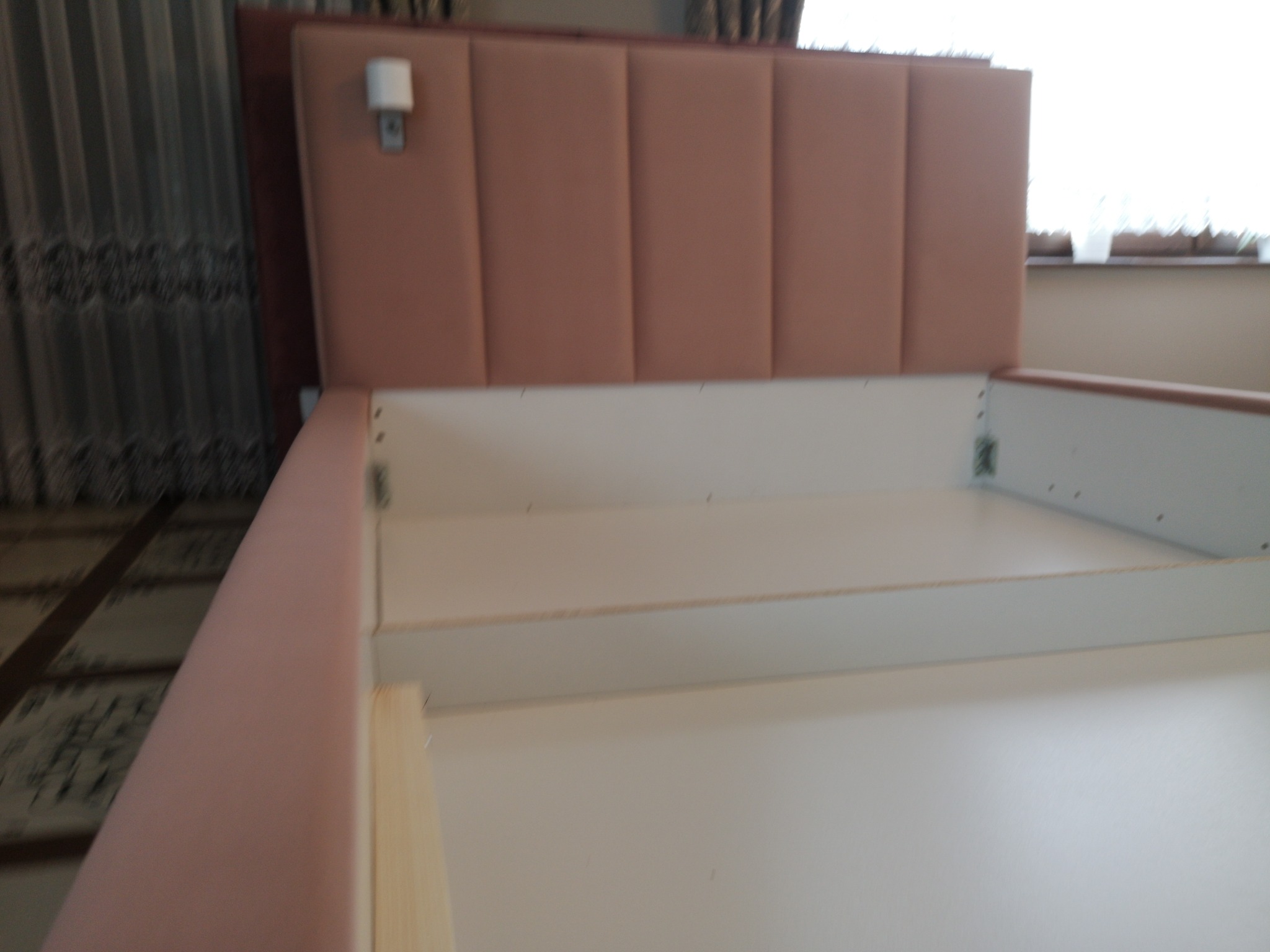 Rama łóżka z tapicerowanym zagłówkiem w odcieniach różu, widoczne elementy montażowe i pusta przestrzeń na materac.