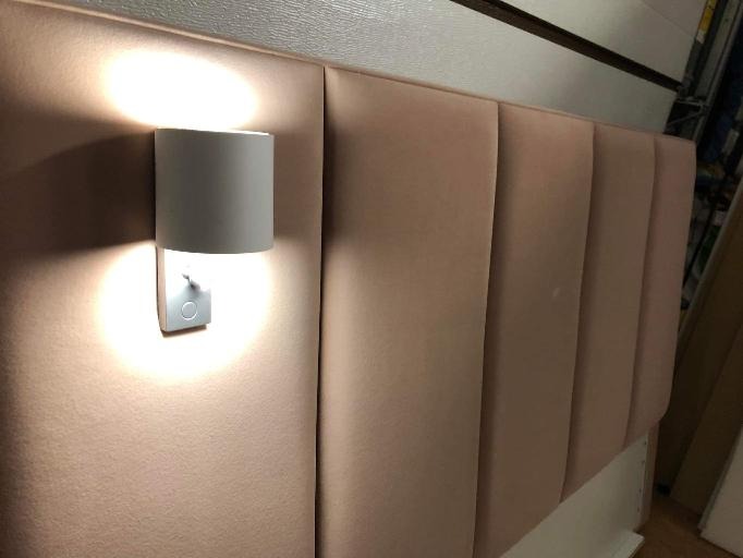 Tapicerowany zagłówek łóżka w odcieniach pudrowego różu z panelem ściennym i zamontowaną nowoczesną lampką nocną.