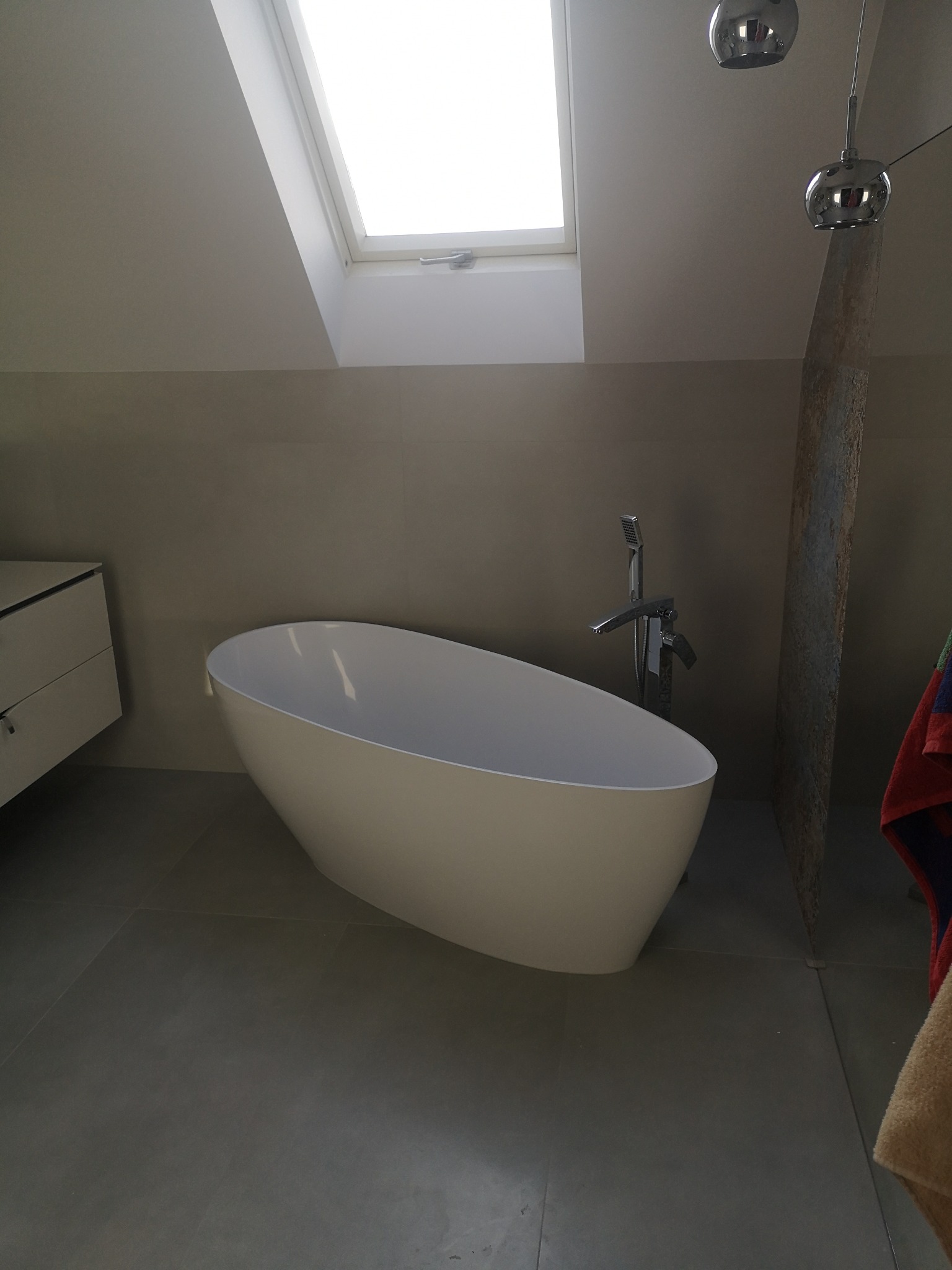 Nowoczesna łazienka z wolnostojącą wanną, minimalistyczną armaturą i oknem dachowym zapewniającym naturalne światło.