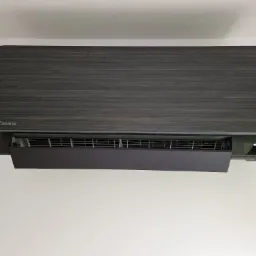 Czarny klimatyzator Daikin z panelem imitującym drewno, zamontowany na białej ścianie, widok z dołu.